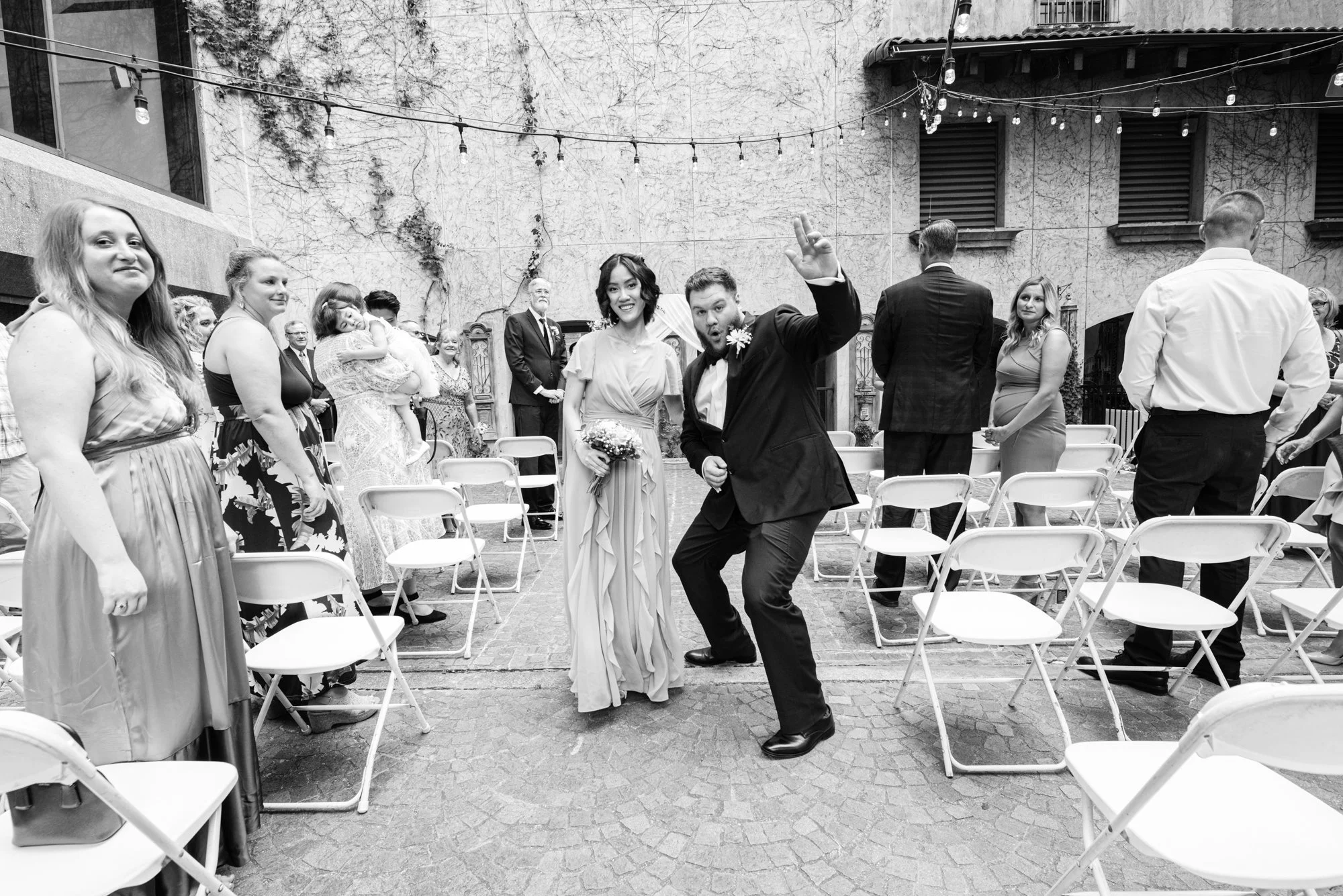 A bridesmaid and groomsman walk playfully down the ceremony aisle, smiling and celebrating as guests look on. The candid energy reflects the joy and personality woven throughout the wedding day.
