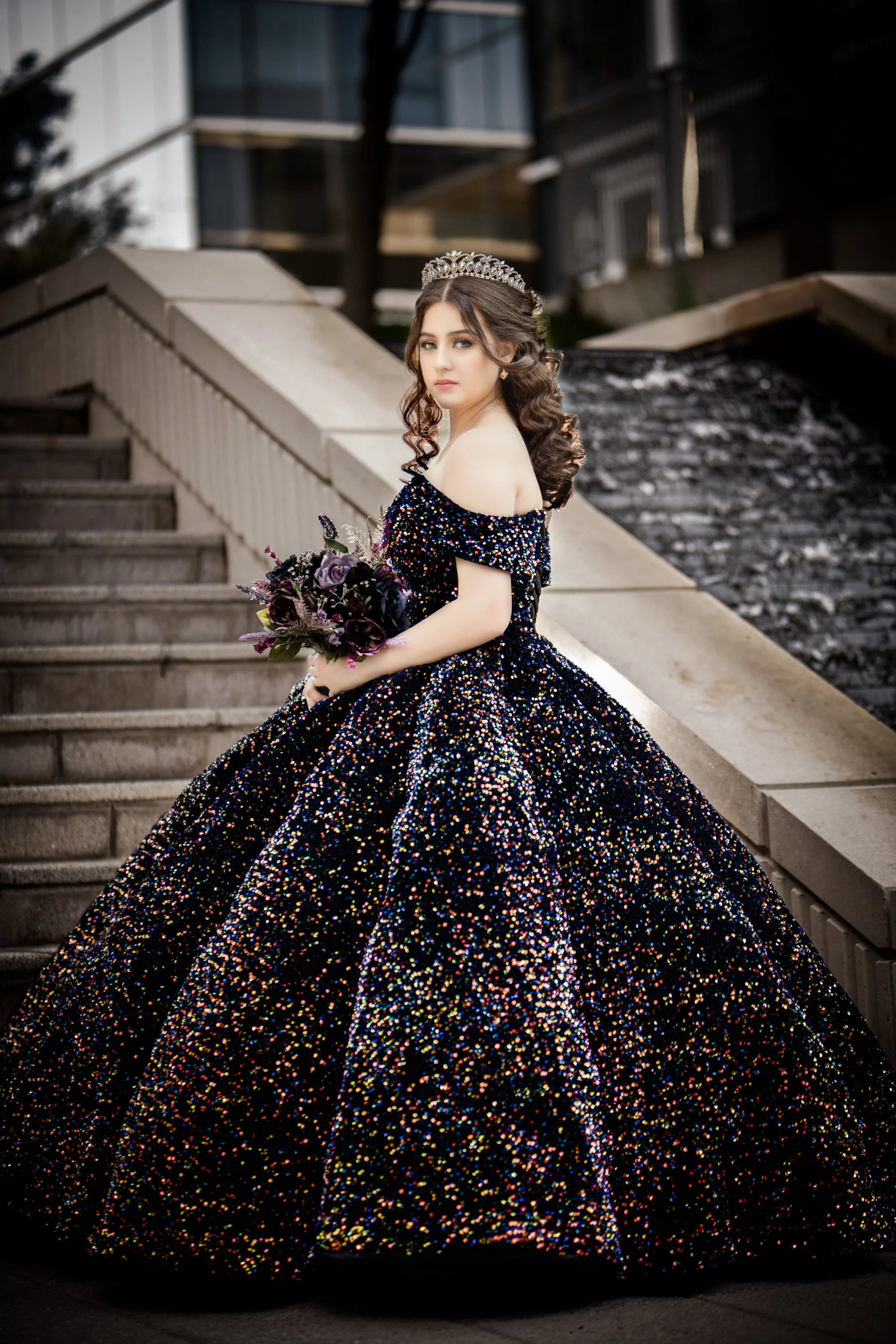 Quinceañera portrait of a young woman in a black gown and crown on stone steps.