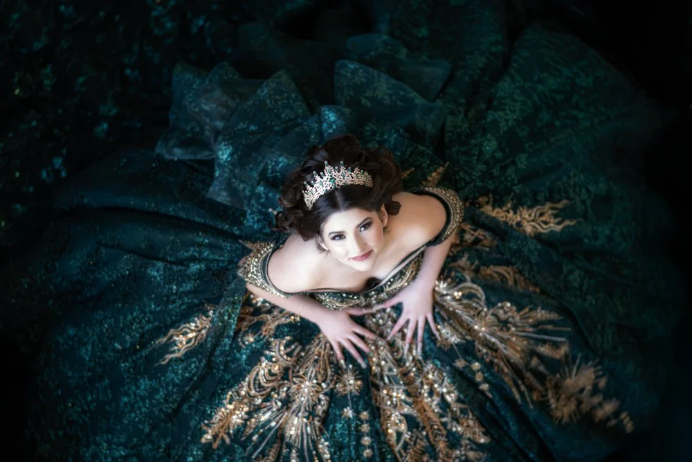 An artistic overhead portrait of Angelina Scott wearing a luxurious emerald and gold Quinceañera gown with a sparkling crown. The dramatic composition highlights the intricate details of the dress while creating a regal and unforgettable image.