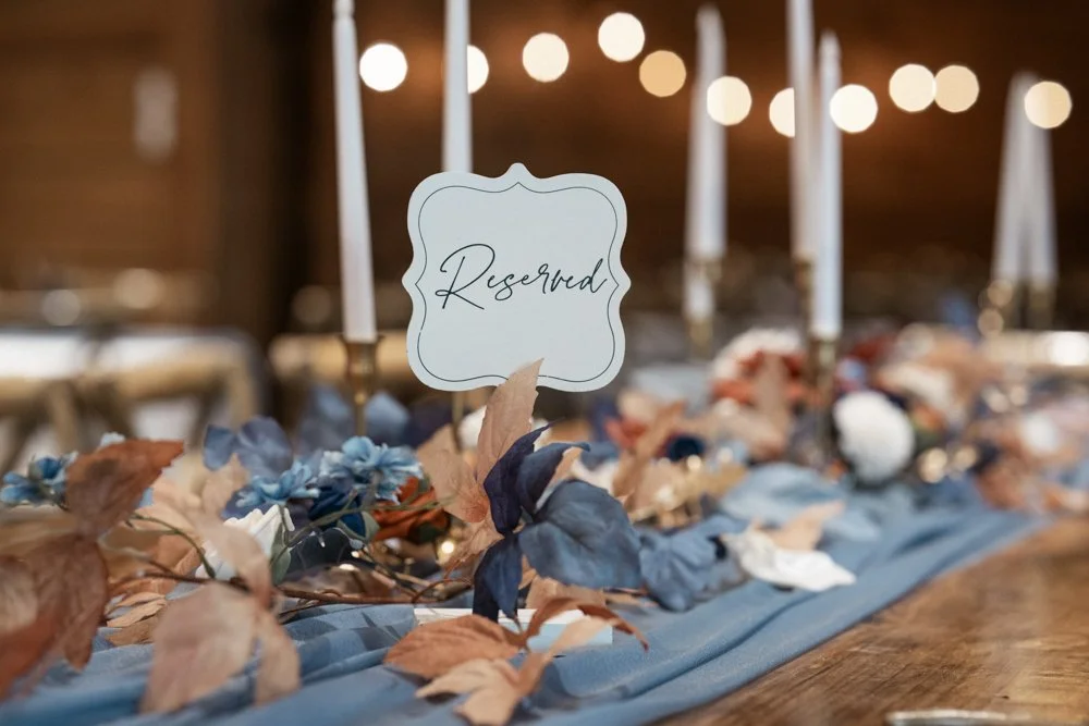 Reserved wedding reception table decorated with blue flowers, candles, and elegant rustic centerpiece decor.