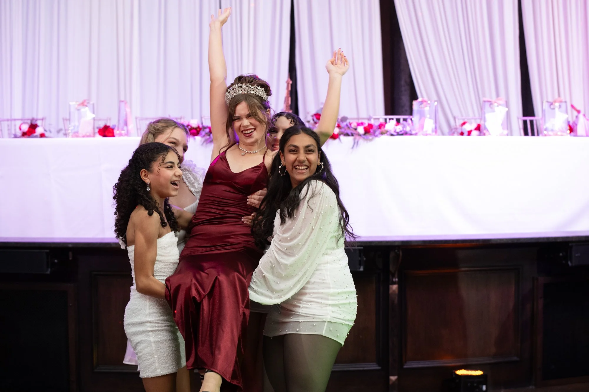 The energy of the night comes alive as Alana is lifted by her friends in pure celebration. With her arms raised and laughter filling the room, the moment reflects the joy and excitement that makes a Quinceañera unforgettable.