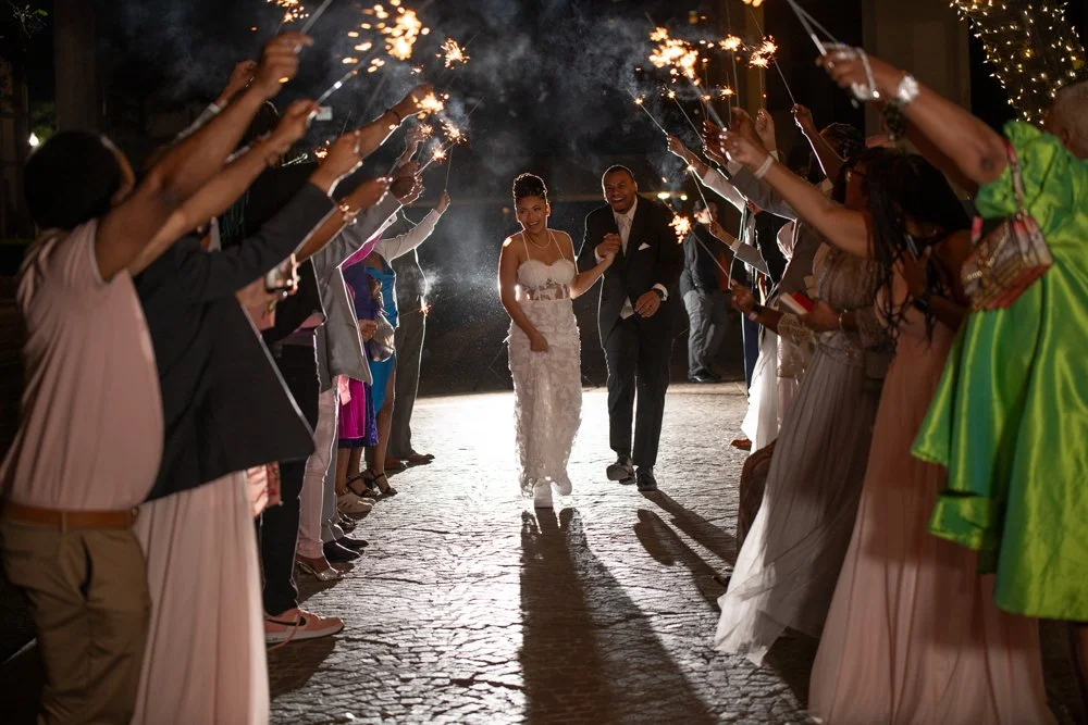 Bride and groom walking through a crowd holding sparklers during wedding celebration at night.