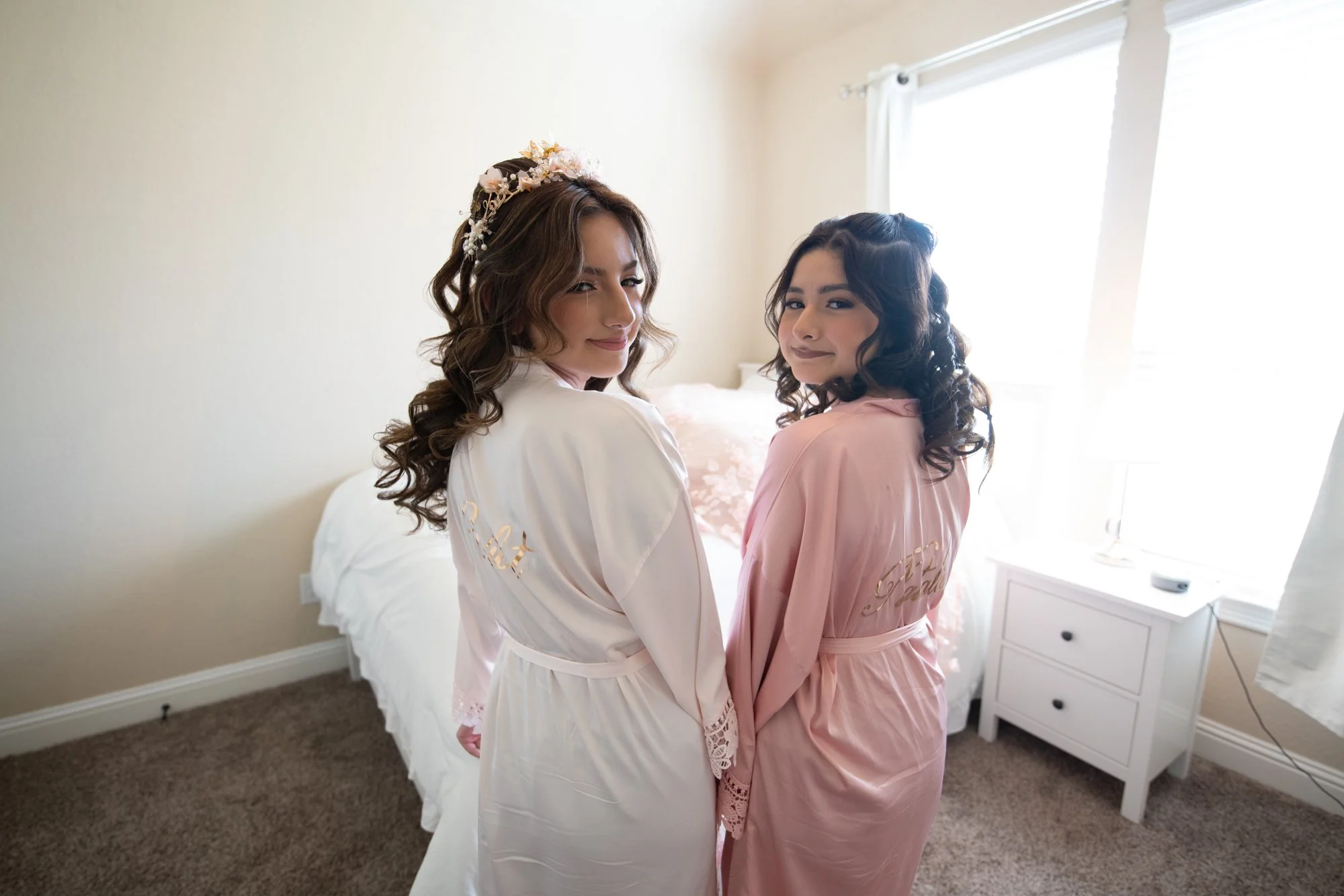 Pure Quince vibes. The birthday girl and her best sister turn over their shoulders in matching satin robes, glowing in soft window light. The quince and personalized robe detail adds a playful, celebratory feel to this getting-ready memory.