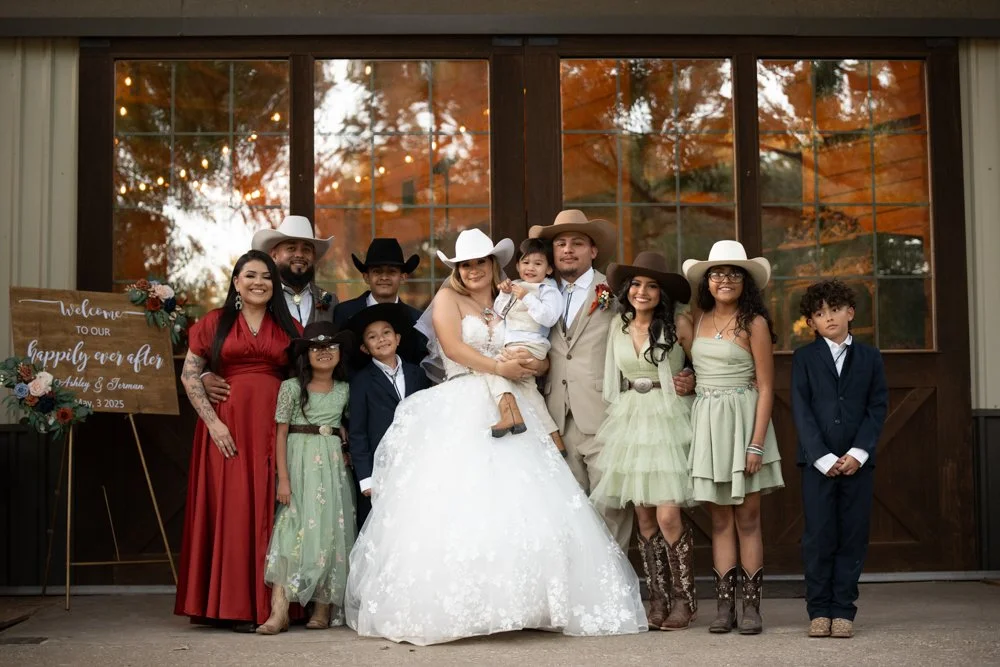 Ashley and Jerman pose with their family outside their Texas ranch wedding venue, celebrating the beginning of their new life together.
