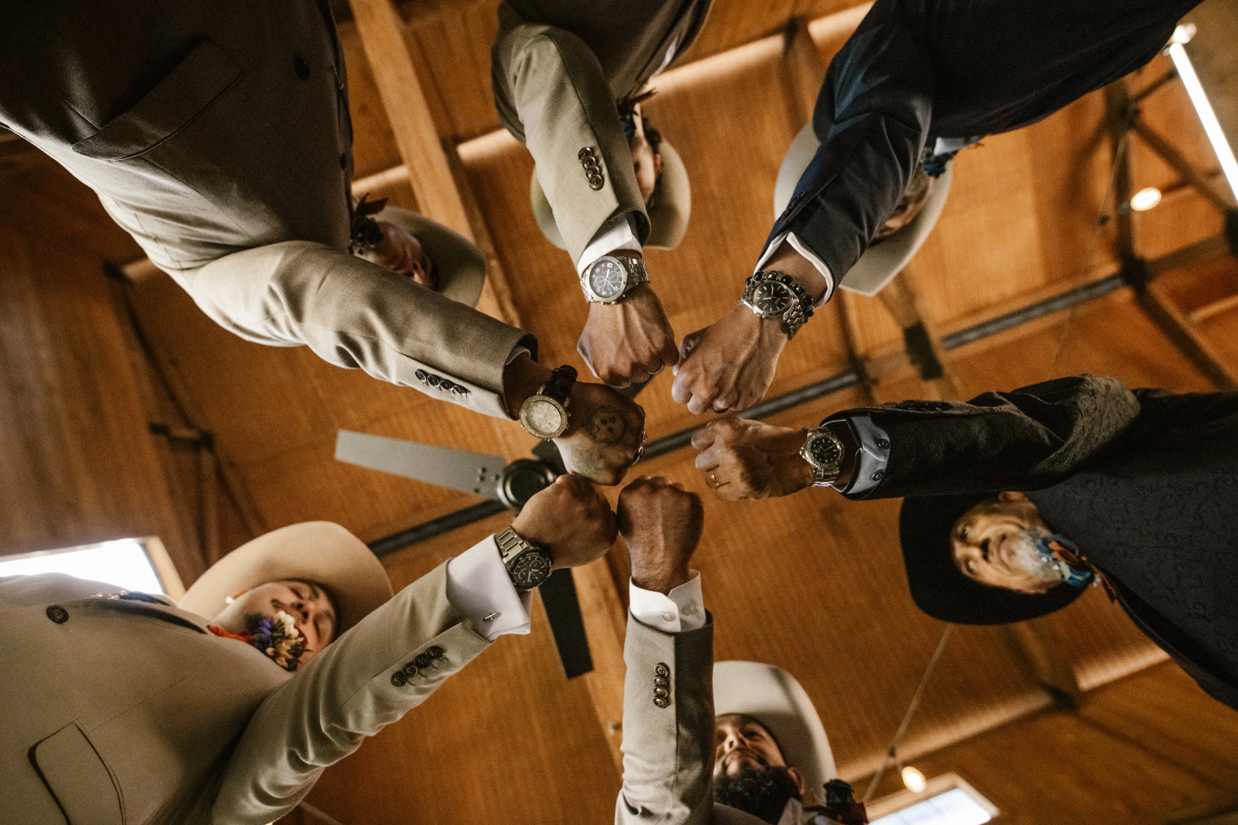 Groomsmen gather in a powerful circle, fists joined together before the ceremony, symbolizing brotherhood, unity, and support on the wedding day.