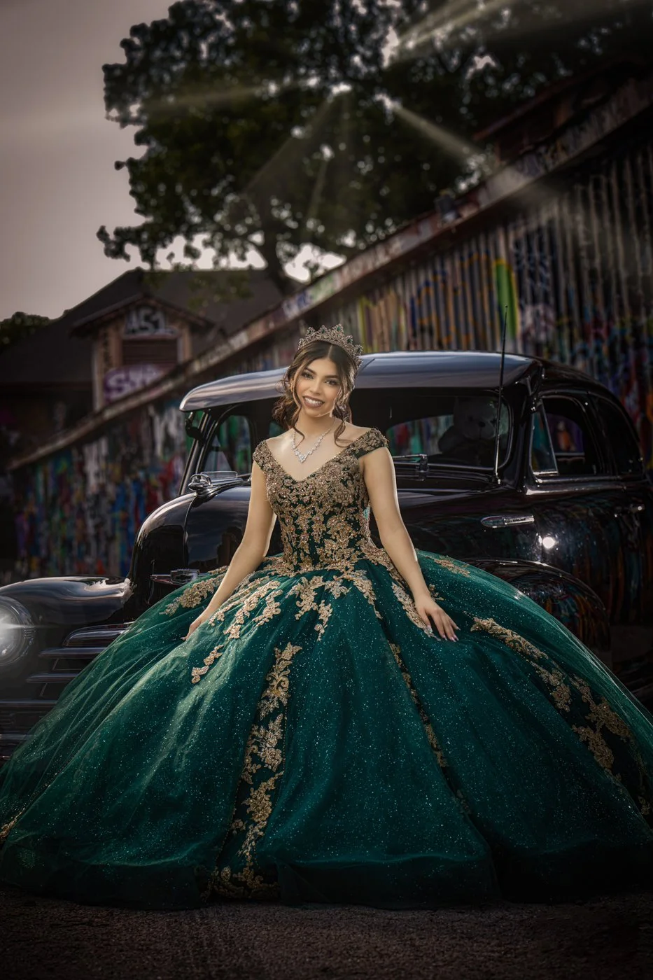 Quinceañera portrait of a young woman in a green gown posing with a vintage car.