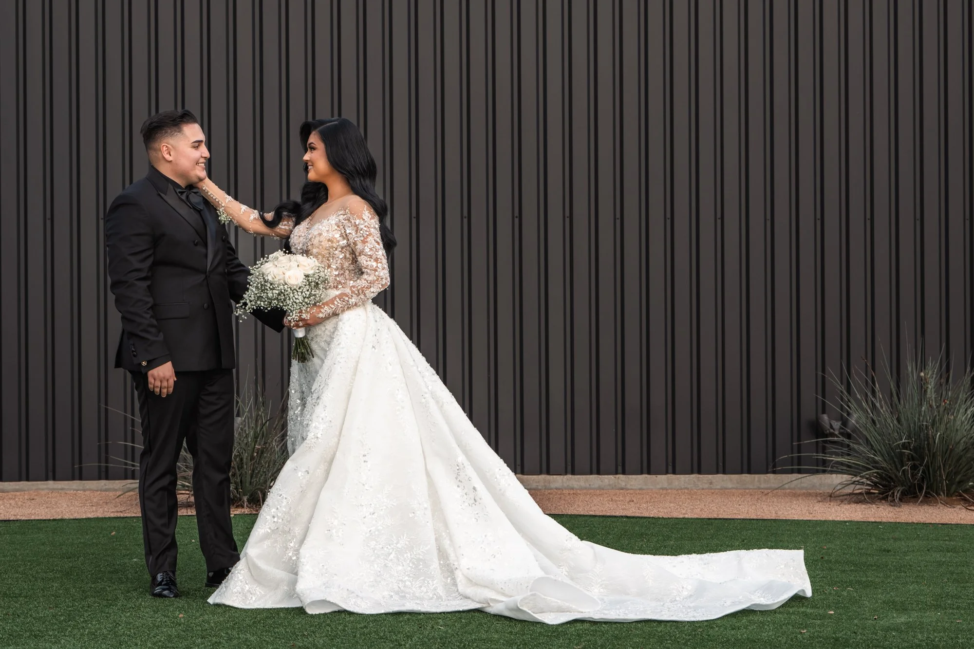 A quiet, intimate portrait of the couple facing one another, capturing connection and anticipation against a modern architectural backdrop that highlights the bride’s flowing gown.