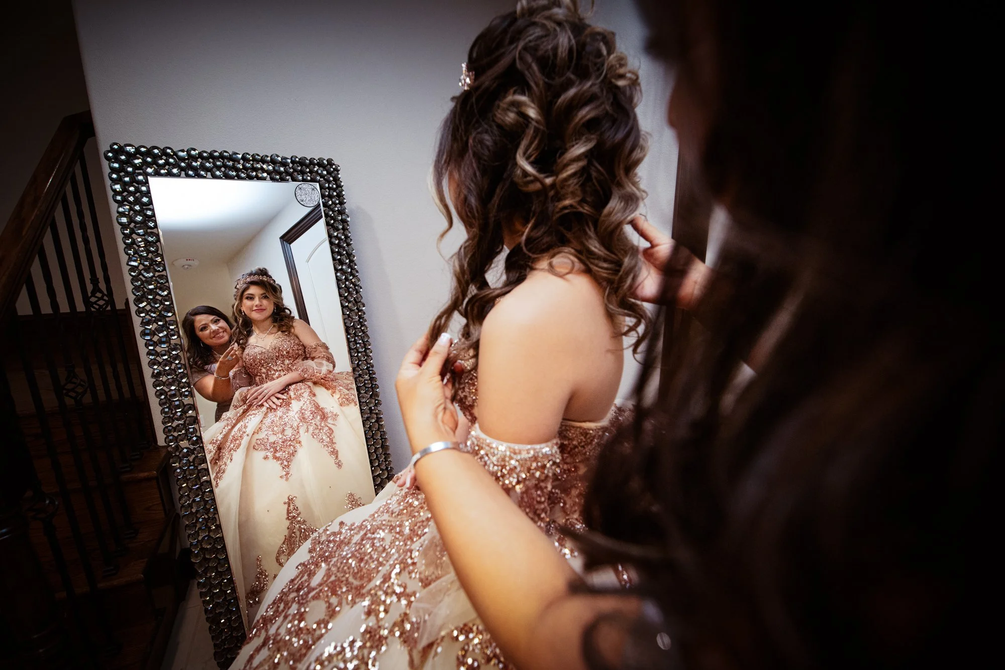 A quiet, emotional getting-ready moment as Katelyn admires her reflection in a statement mirror while her mother lovingly adjusts her curls. Her rose gold embroidered gown sparkles beautifully, capturing both the elegance of the dress and the anticip