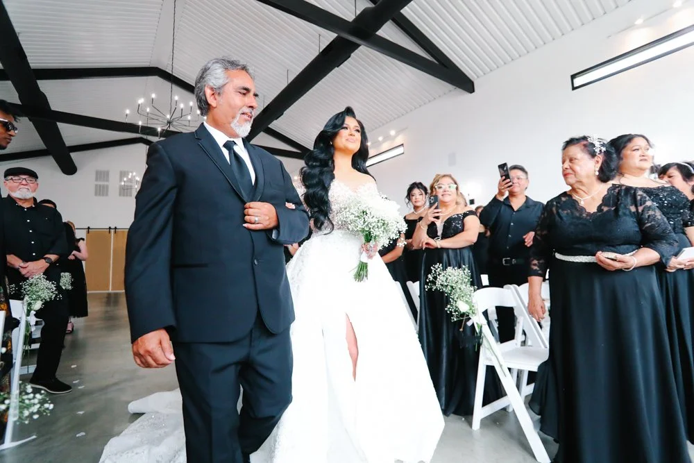 Bride walking down the aisle with her father during an emotional indoor wedding ceremony surrounded by family and friends.