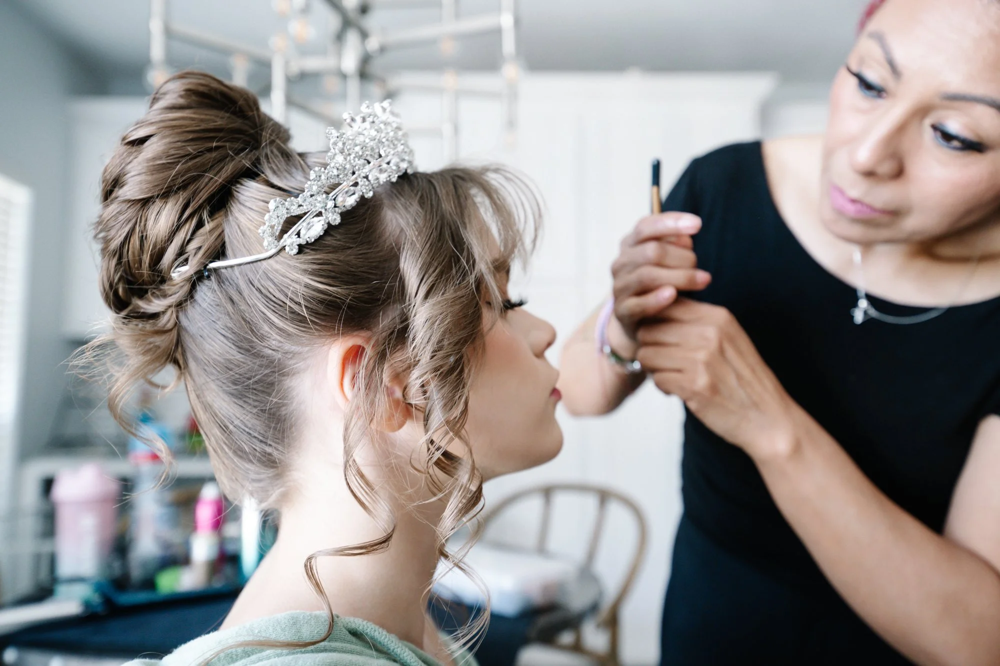 An intimate behind-the-scenes glimpse of Alana during her glam session. As final makeup touches are applied and her tiara sparkles in the light, the image captures the transformation into a true Quinceañera princess ready for her grand celebration.