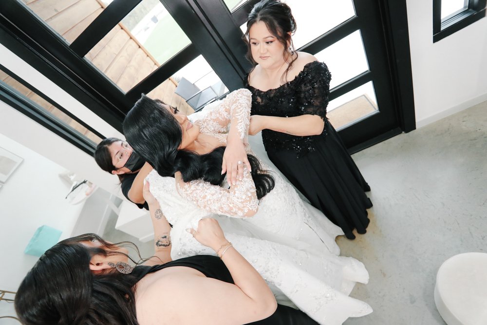 Bride getting dressed with assistance from bridesmaids before her wedding ceremony at a modern wedding venue.