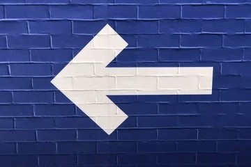 White left-pointing arrow painted on a blue brick wall.