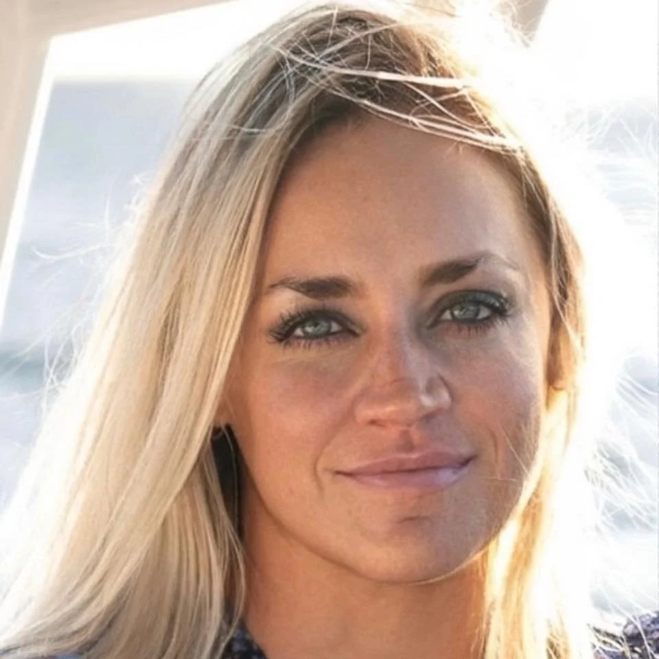 Close-up of a woman with long blonde hair, blue eyes, and light makeup, smiling softly.