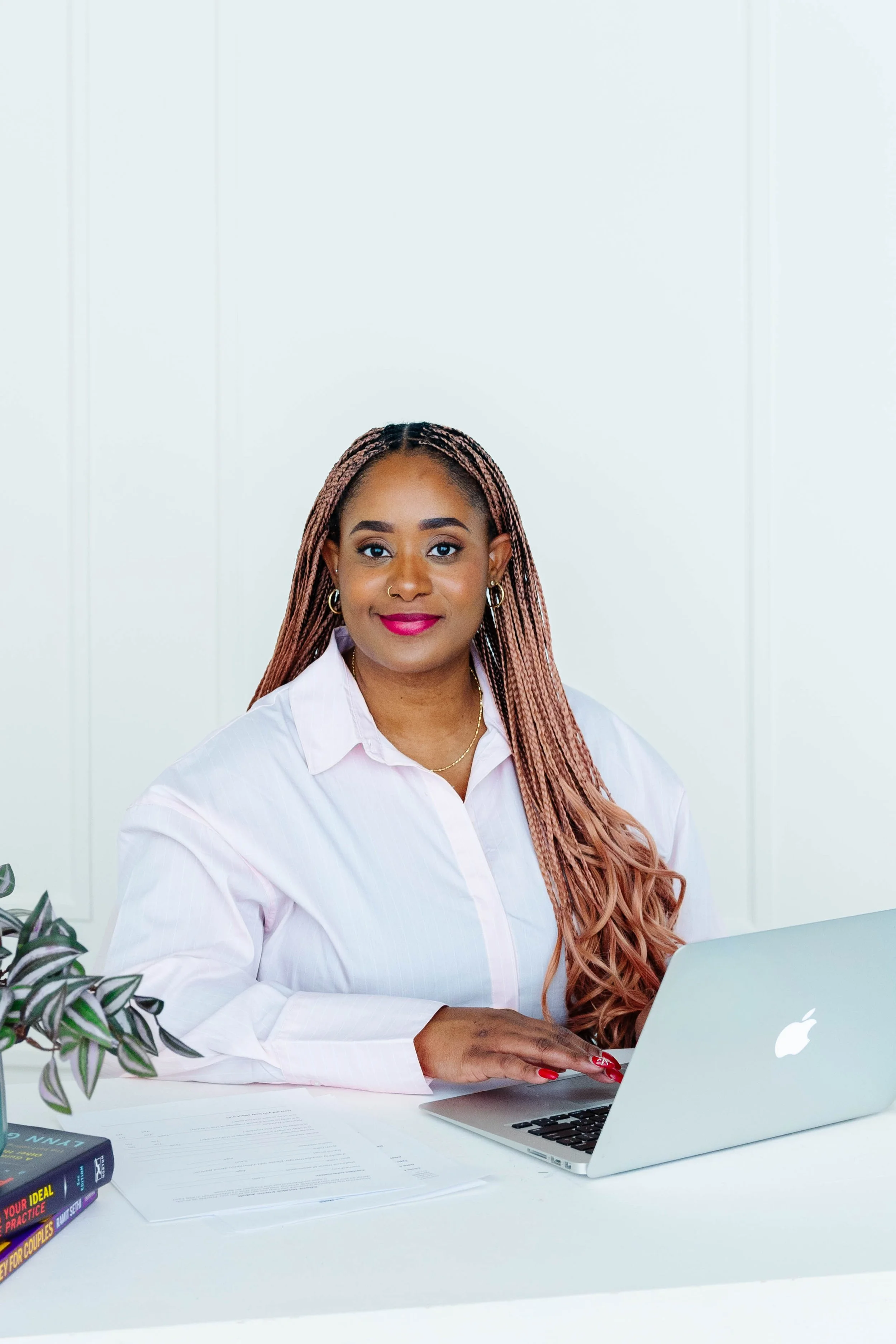 Smiling Black woman with long braids working on a laptop at a white desk