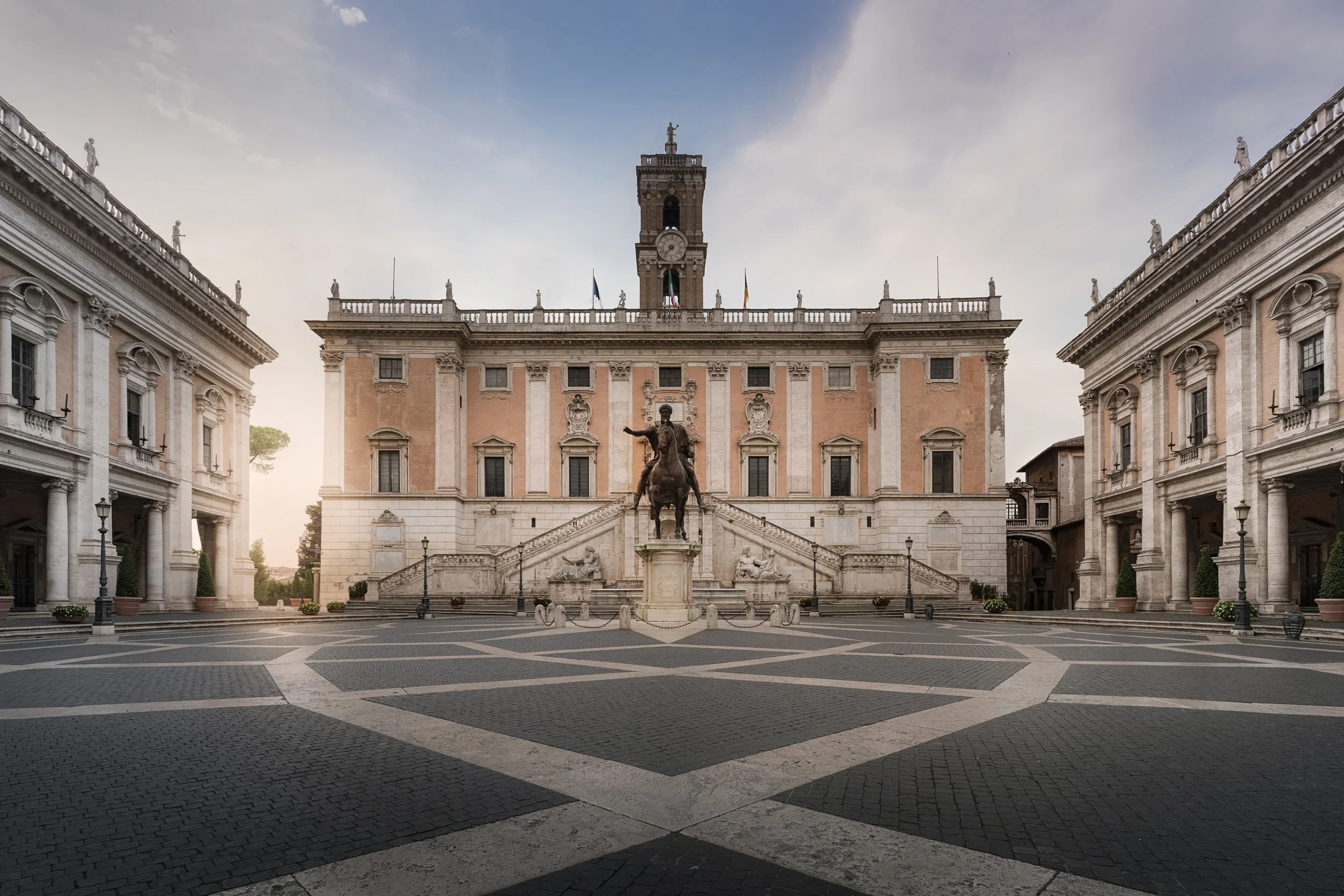 Empty historic square with grand neoclassical buildings and statue of a man on horseback in the center.