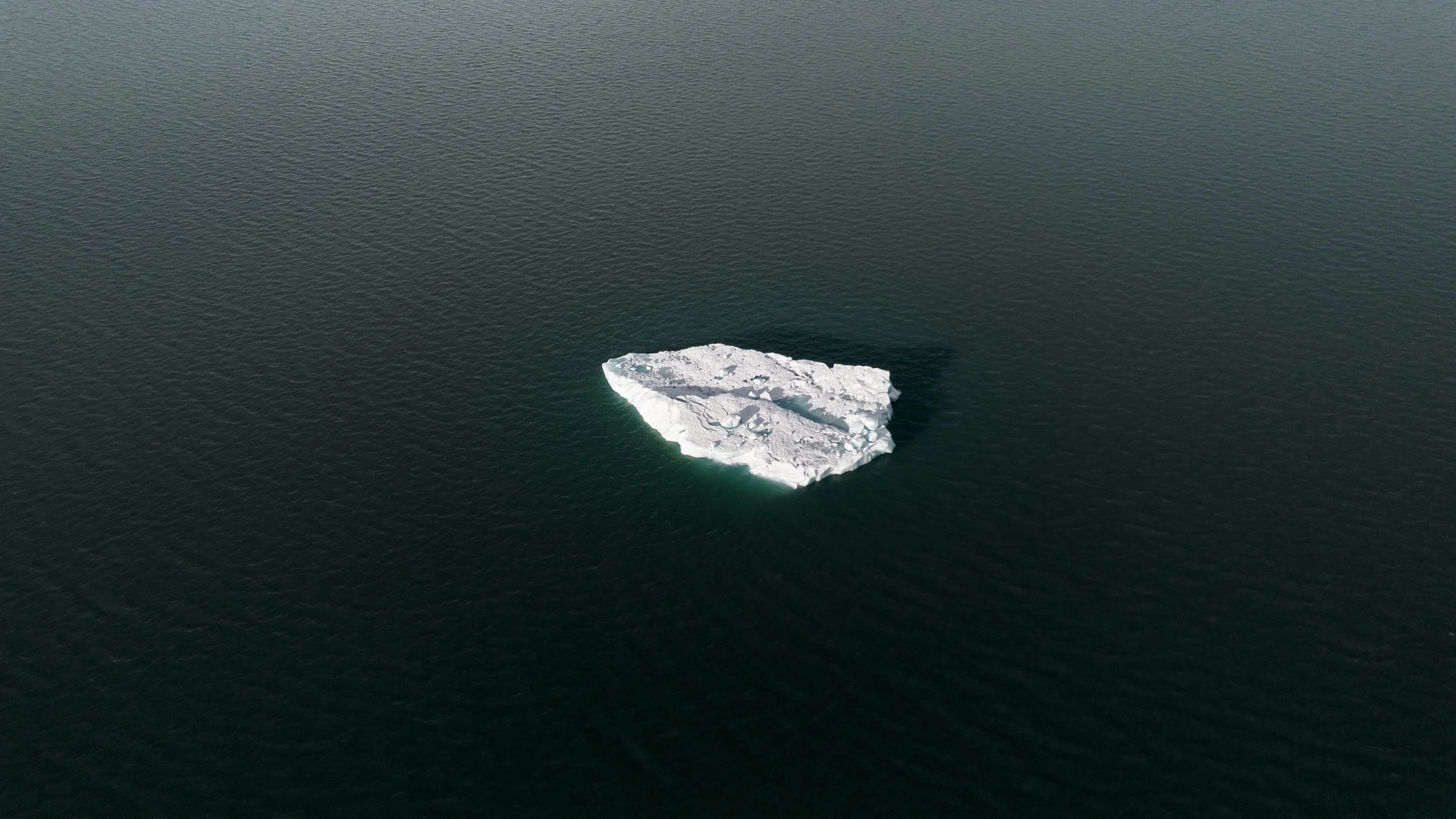 A lone iceberg floating in dark ocean water.
