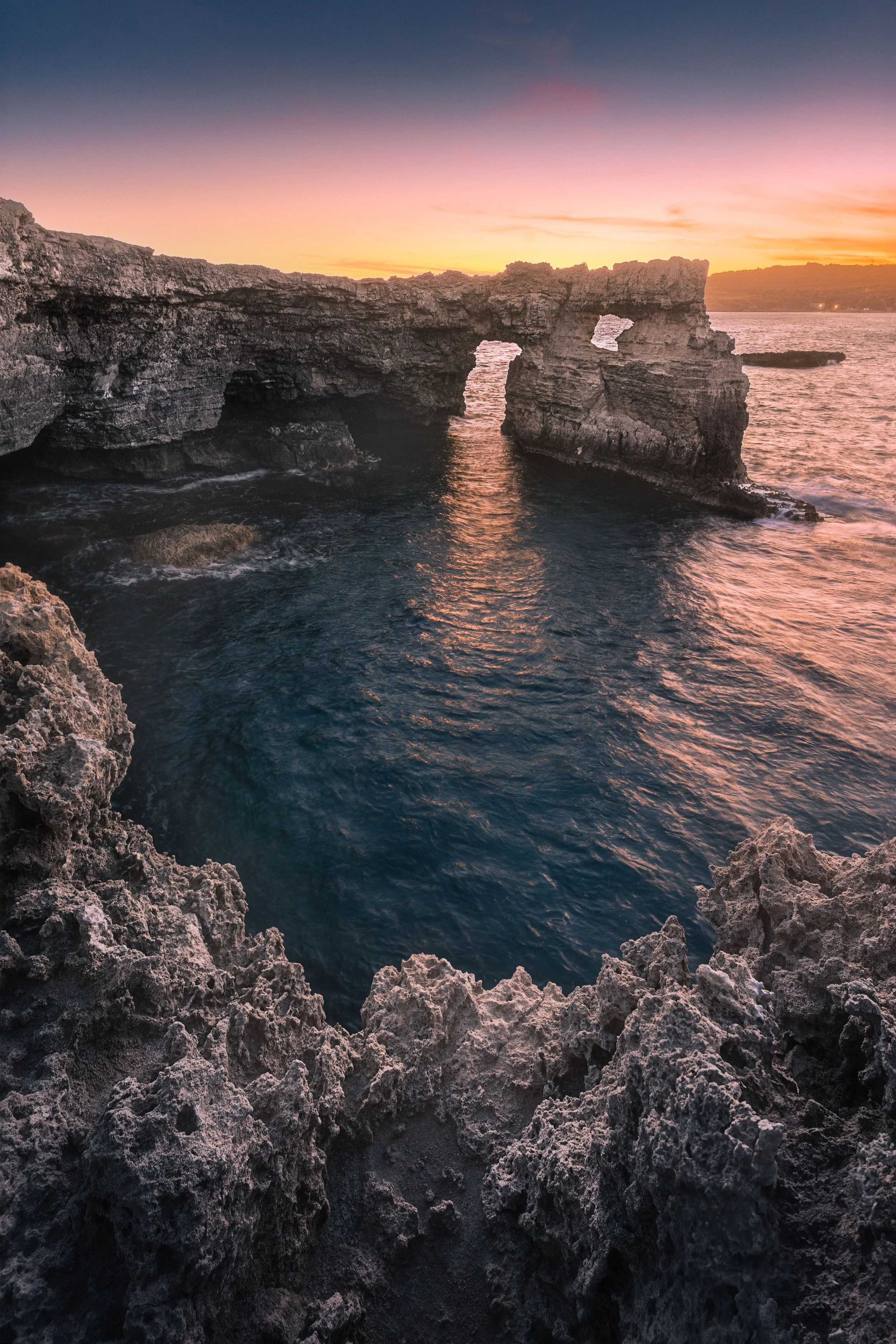 Rocky coastal cliffs and natural arches at sunset over the ocean.