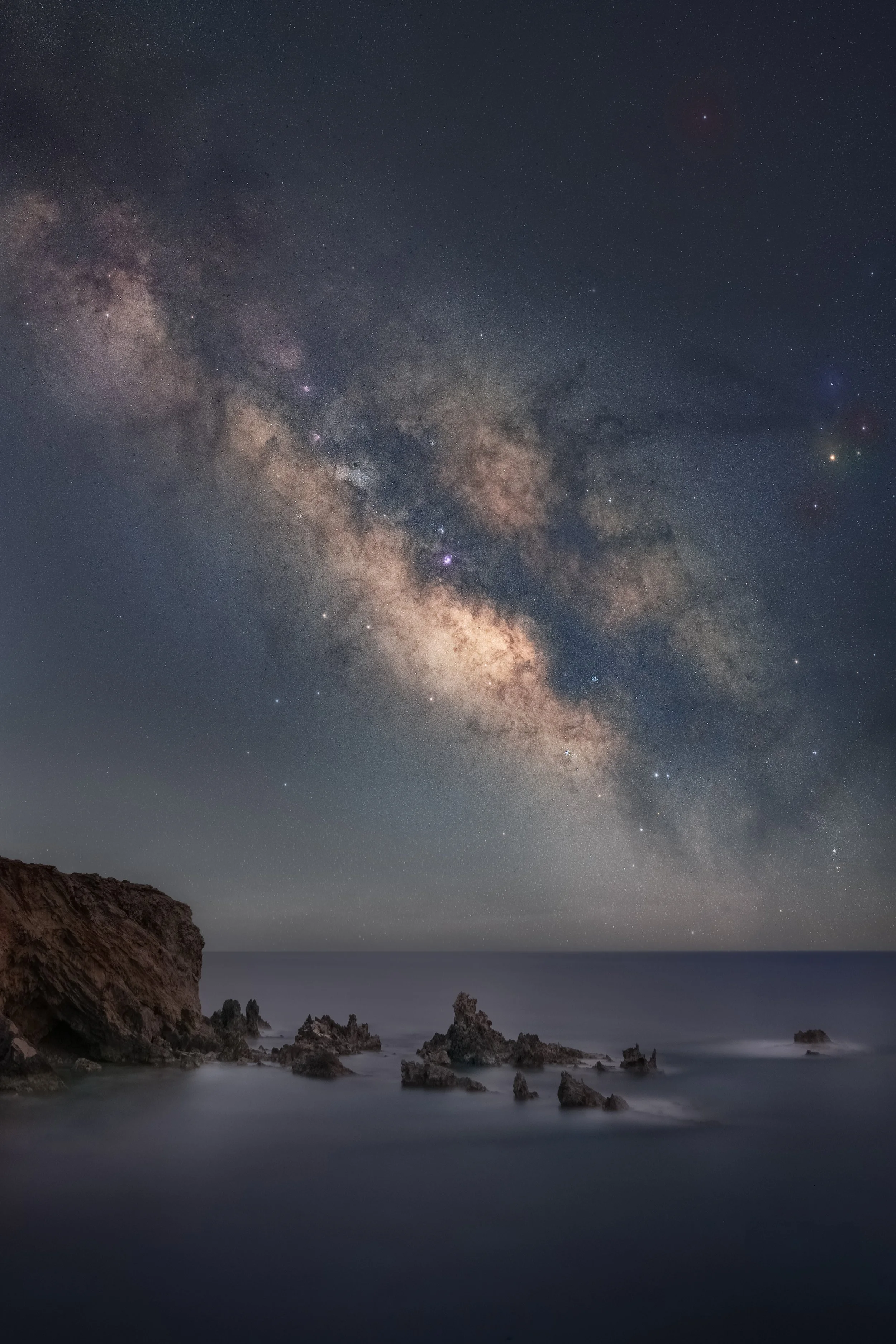 Milky Way galaxy over a rocky coastal landscape at night.