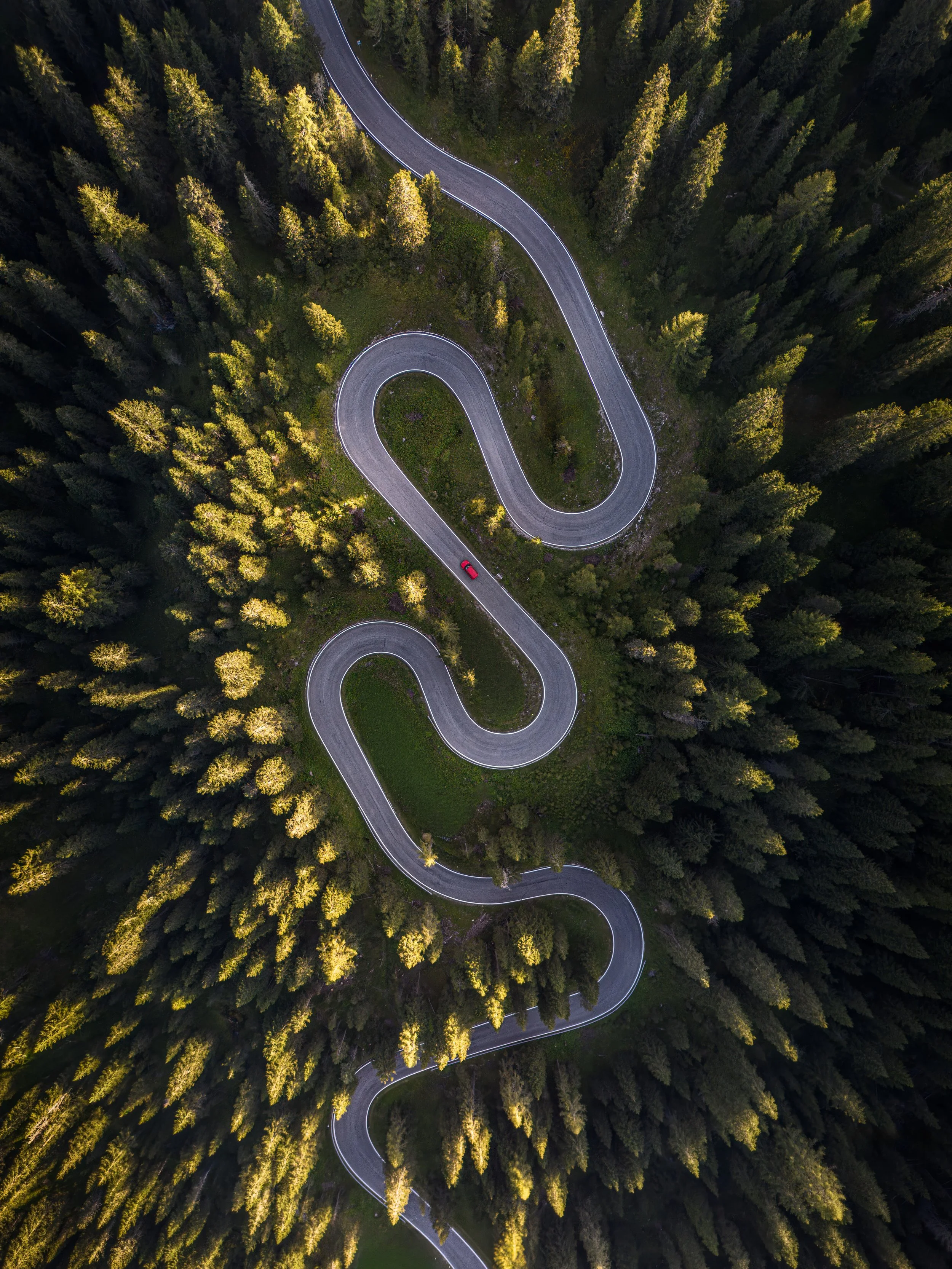An aerial view of a winding mountain road surrounded by dense green forest.