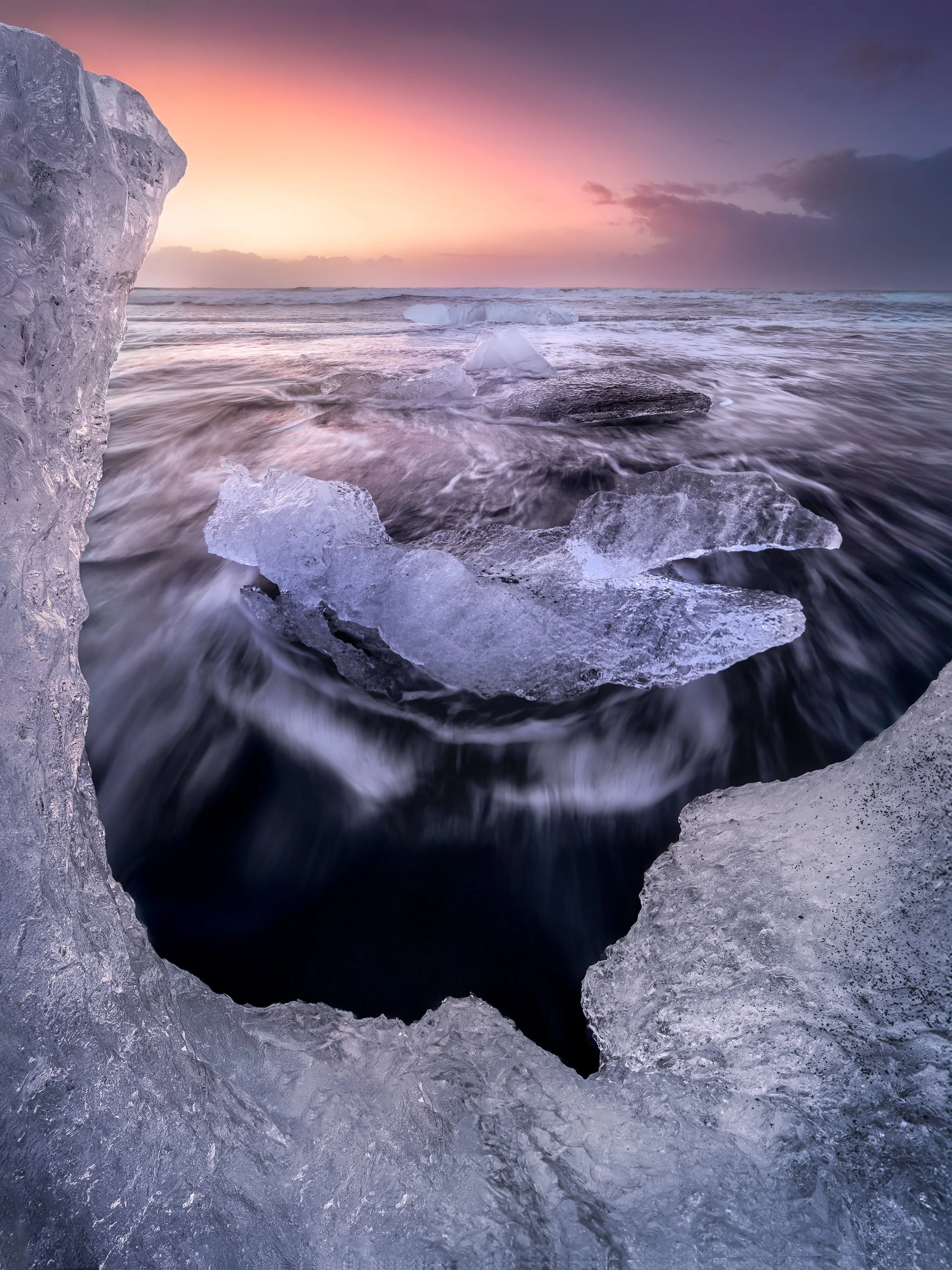 Icebergs on a beach during sunset, with waves washing around the ice fragments.