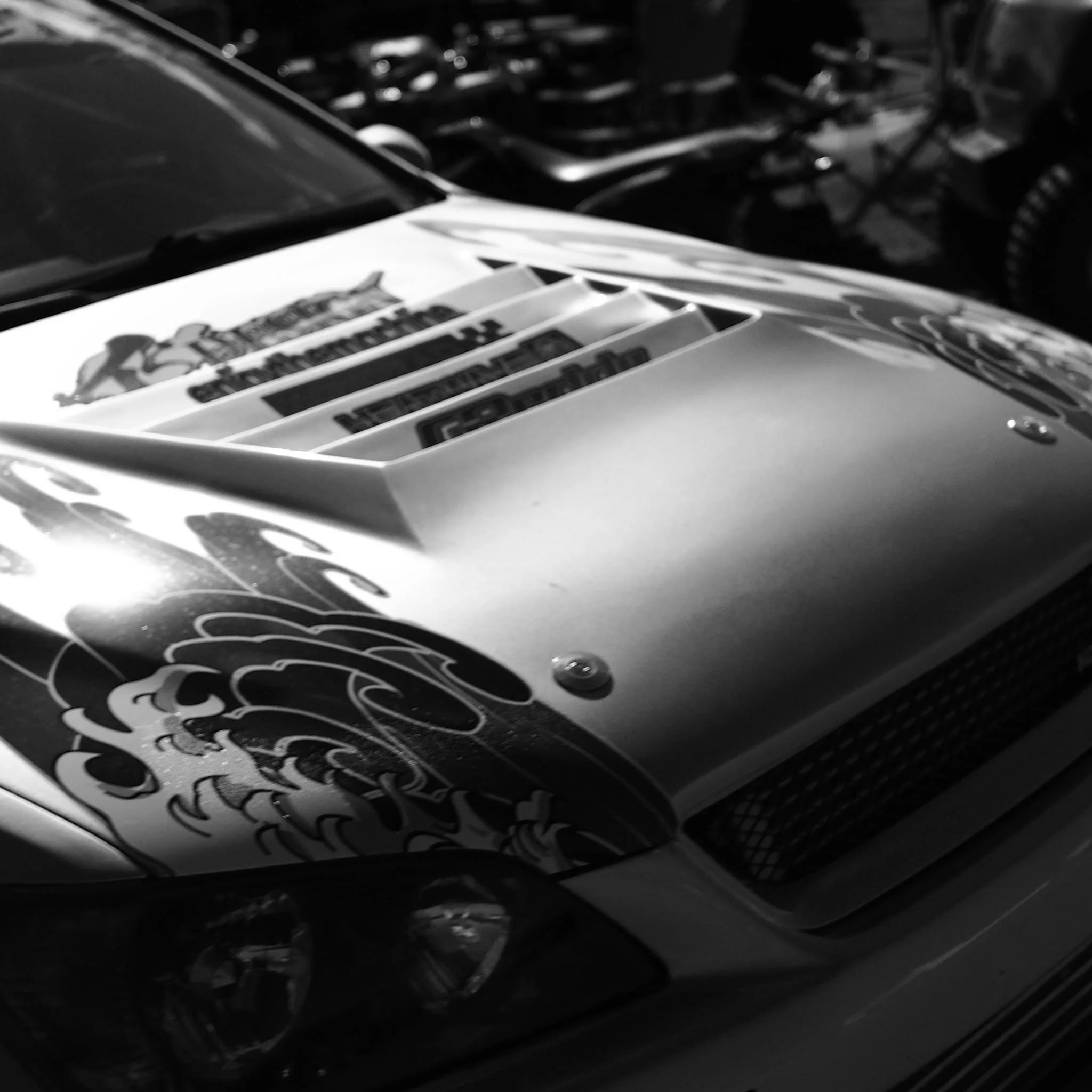 Close-up of the hood of a race car with decorative stickers and an air intake vent.