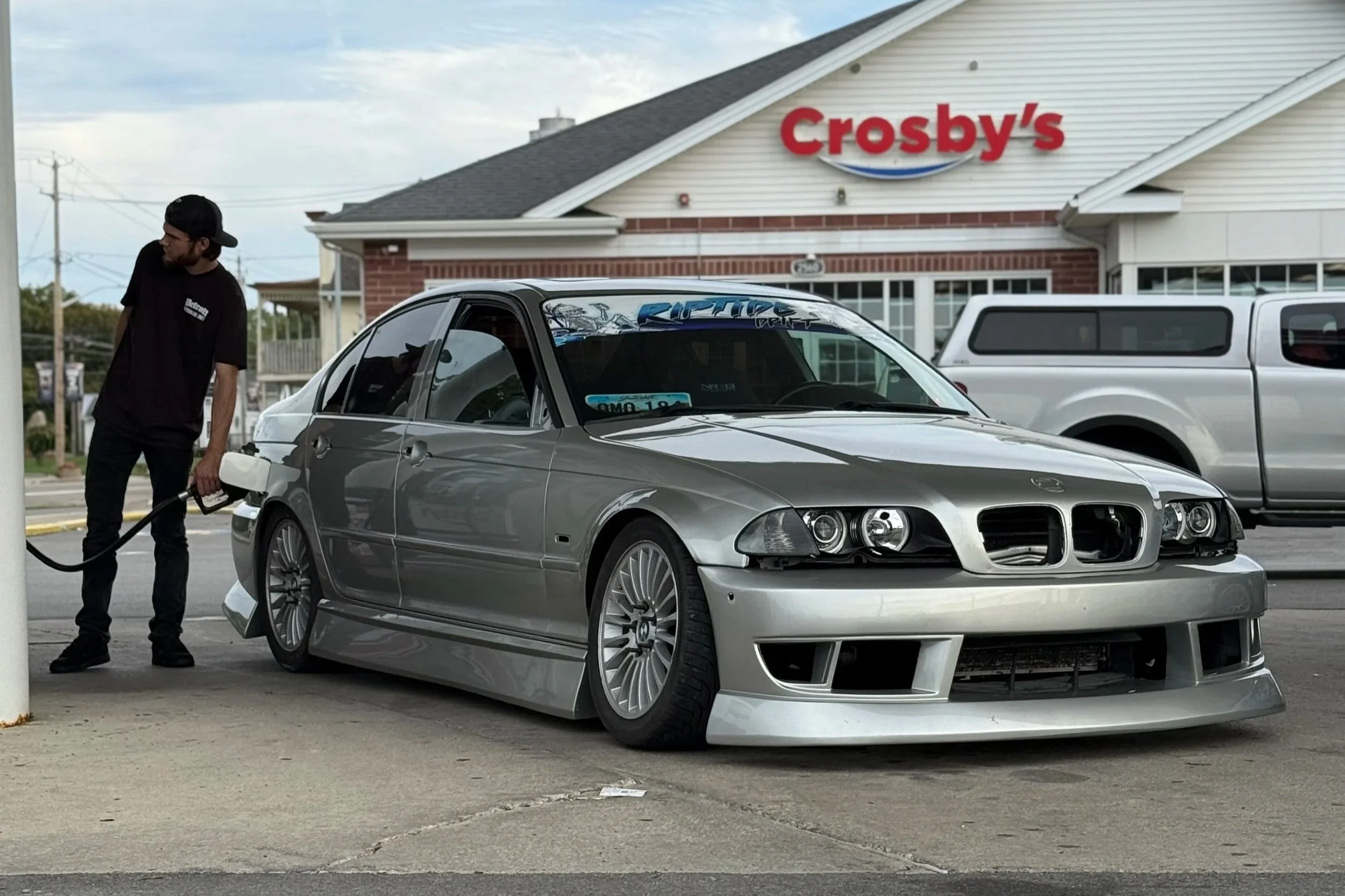 Man filling a silver BMW car with fuel at a gas station.