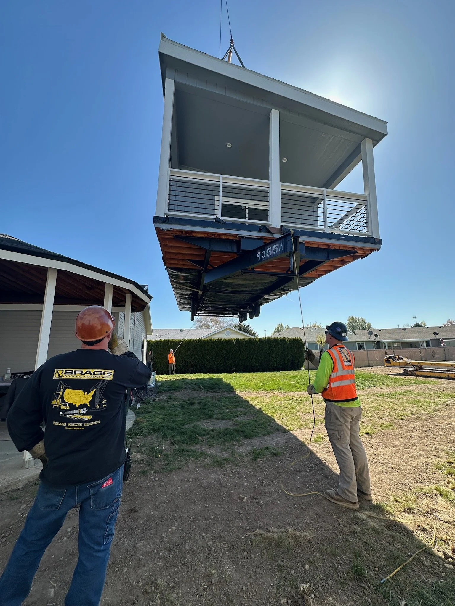 Construction workers are lifting a large modular building or tiny house onto a foundation in a residential area.