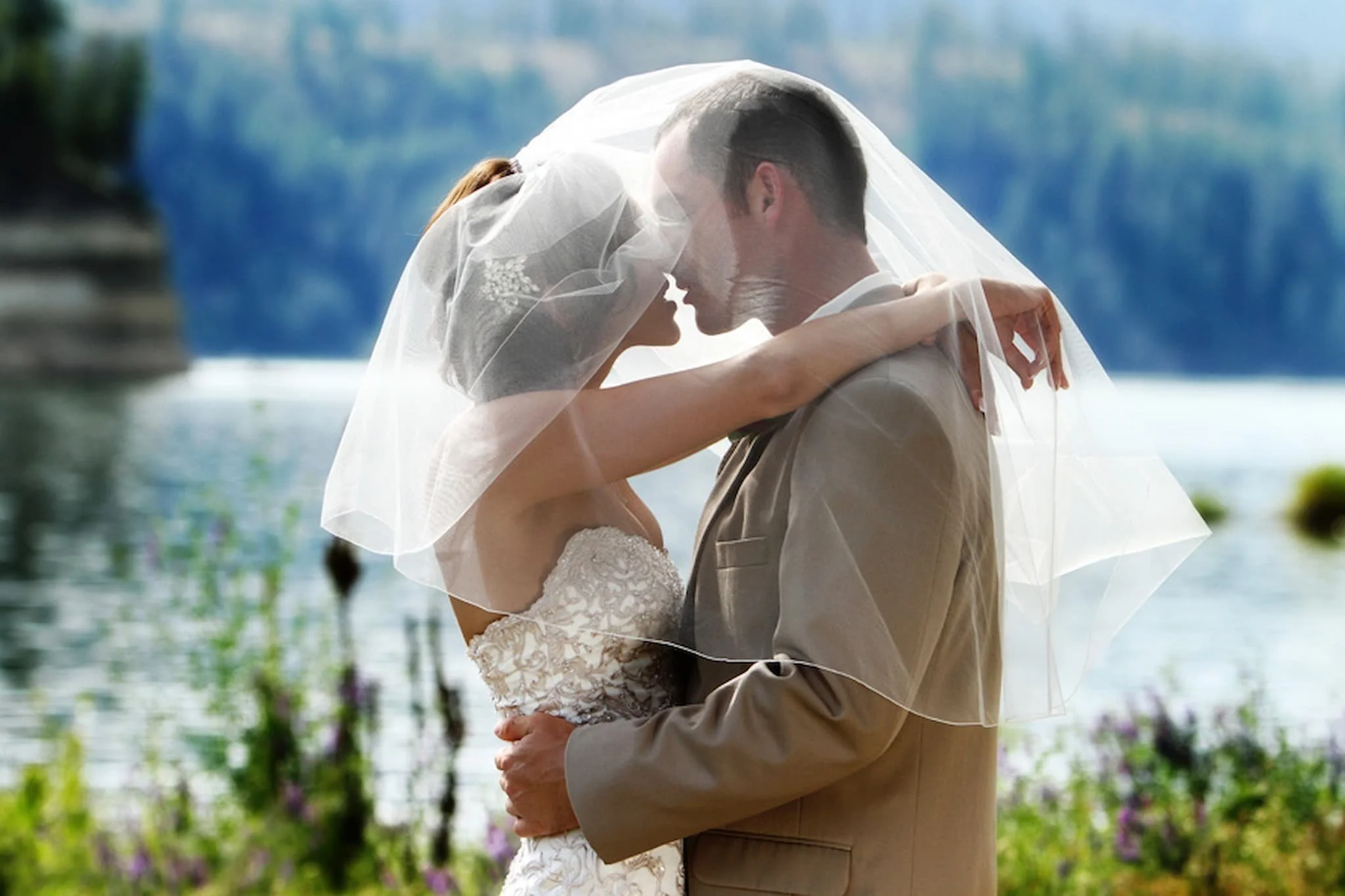 Bride and groom kissing under a flowing veil, with soft light highlighting the intimate, emotional moment.