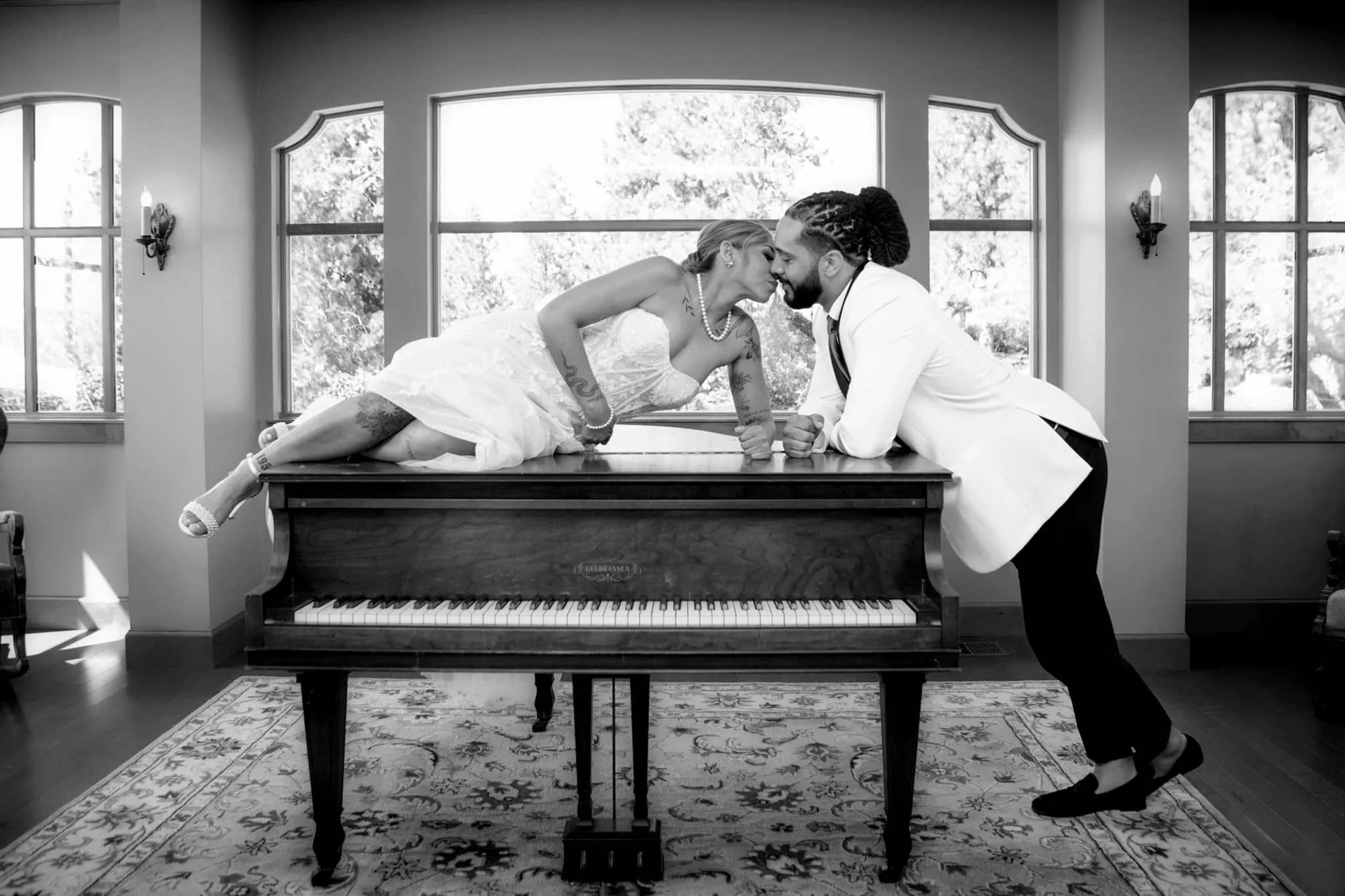 Bride perched on a piano kissing her groom, captured in a creative and romantic wedding moment