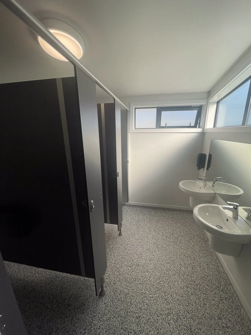 A construction worker in a hoodie and baseball cap working on framing a building's interior with wooden beams, power tools, and construction materials on a makeshift workbench.