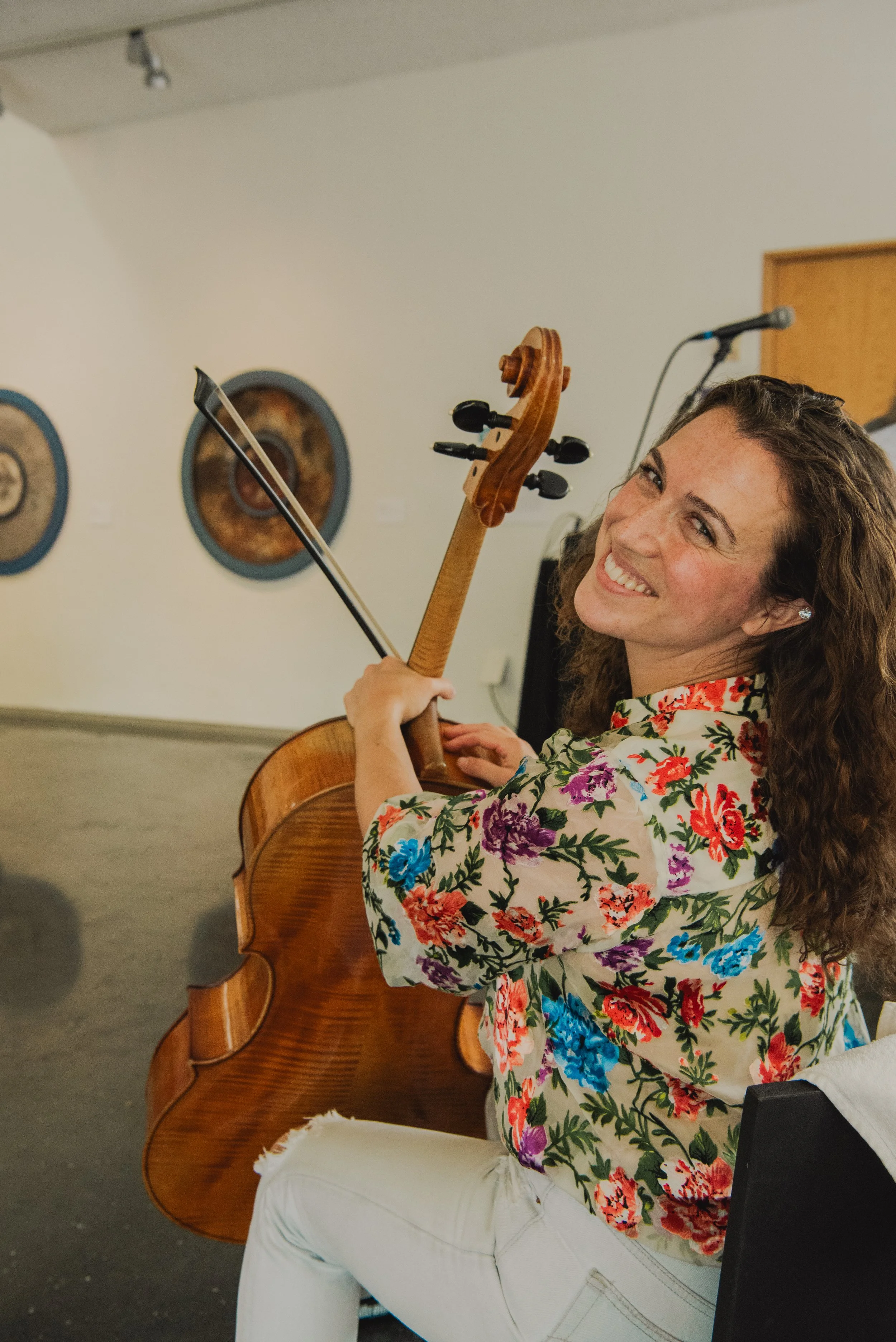 A woman with long curly hair smiling while playing the violin in an indoor setting.