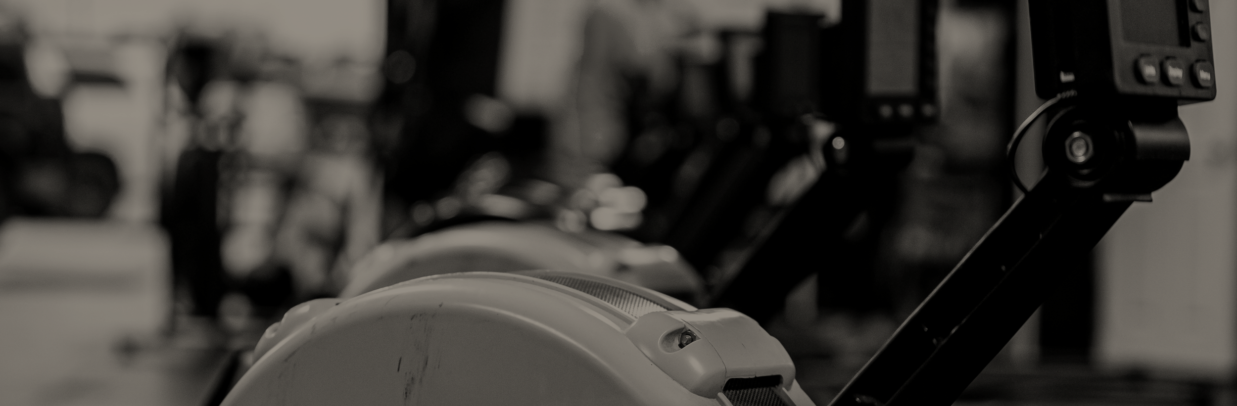 Close-up of exercise equipment, including a rowing machine in a gym, shown in black and white.
