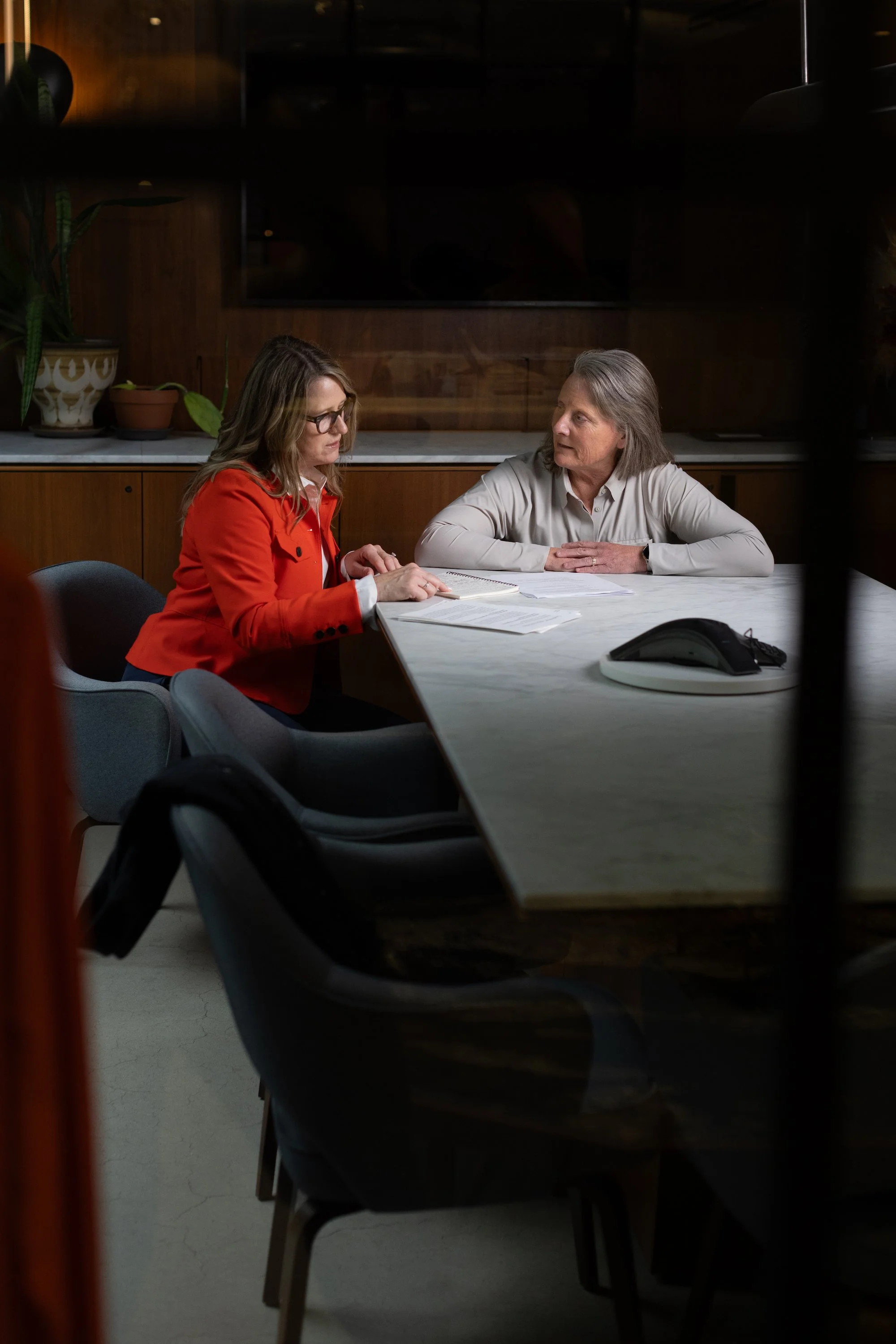 Teri Evans and Gennifer Baker in discussion at a table in a wood-paneled conference room