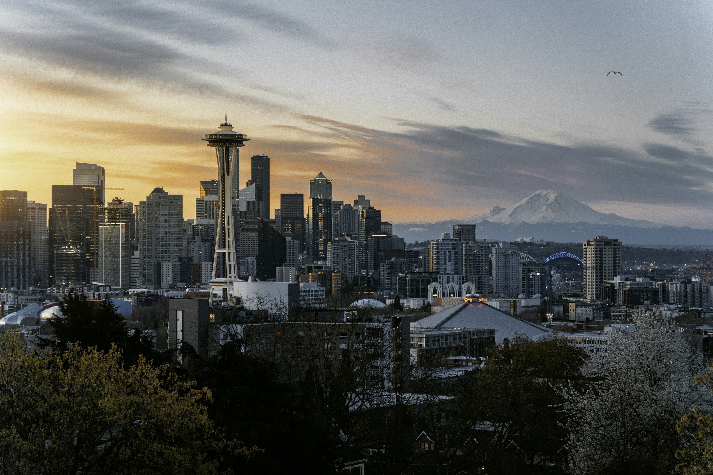Seattle skyline at sunset with Space Needle in foreground and Mount Rainier in background.