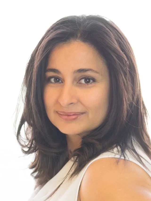 A woman with shoulder-length dark hair and light skin, smiling confidently, wearing a white top, against a plain white background.