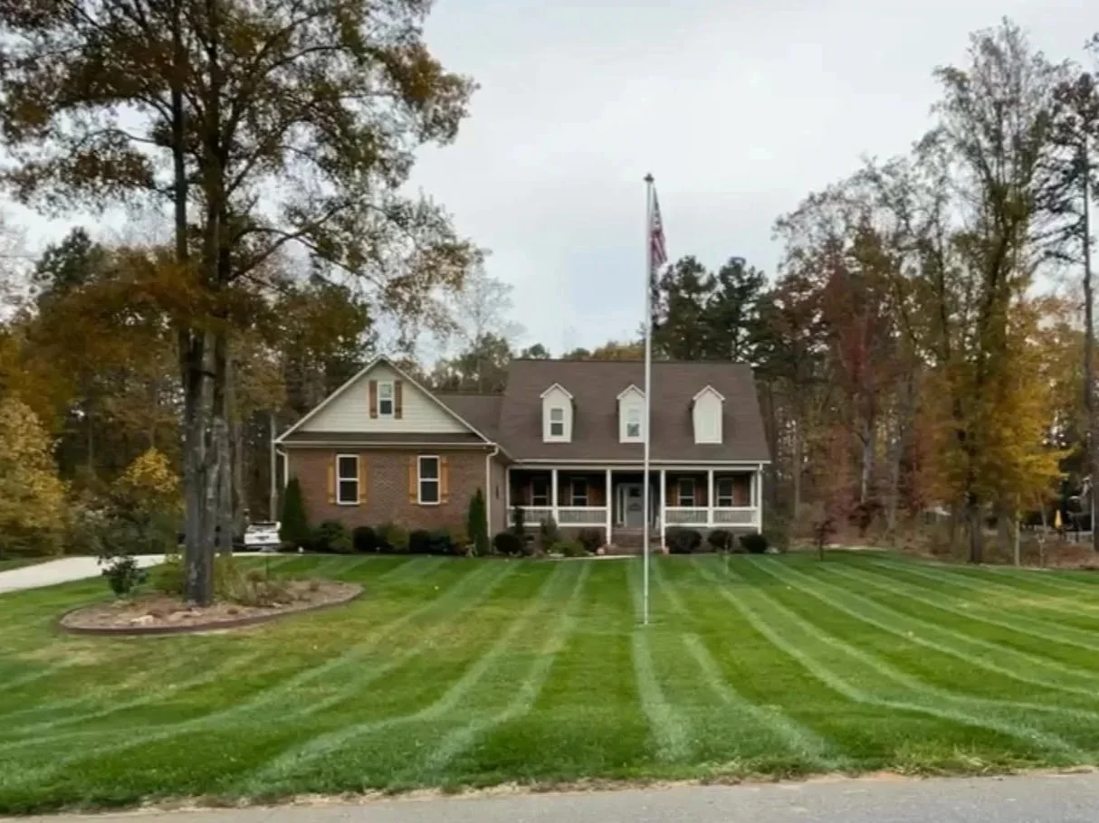 A large house with a front porch, surrounded by trees, with a well-manicured lawn and an American flag on a flagpole in the front yard.