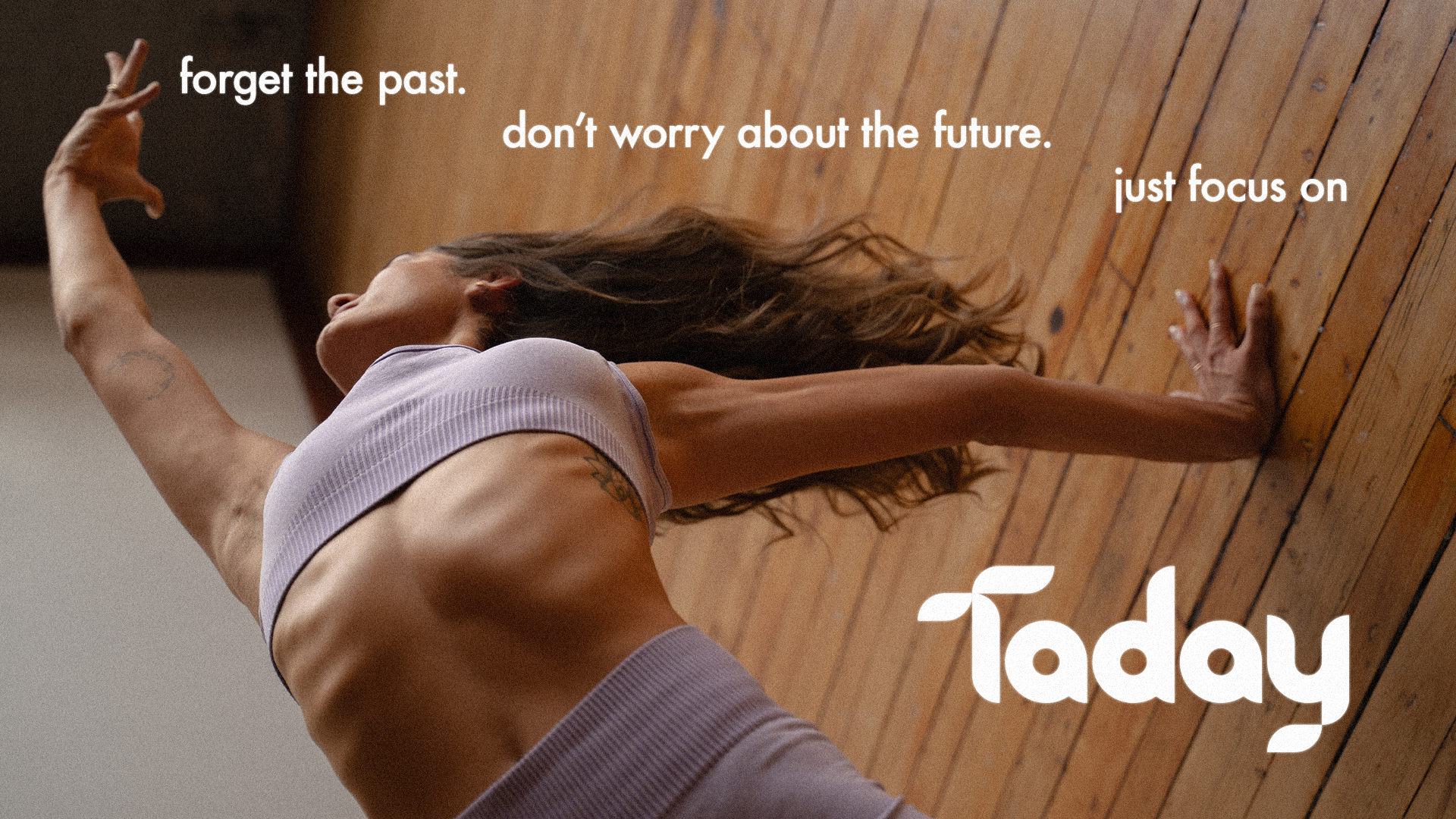 A woman with tattoos practicing yoga on a wooden floor. She is in a side plank pose, wearing a lavender sports bra and leggings. The image includes an inspirational quote, "forget the past. don’t worry about the future. just focus on", and the word "Taday" at the bottom.