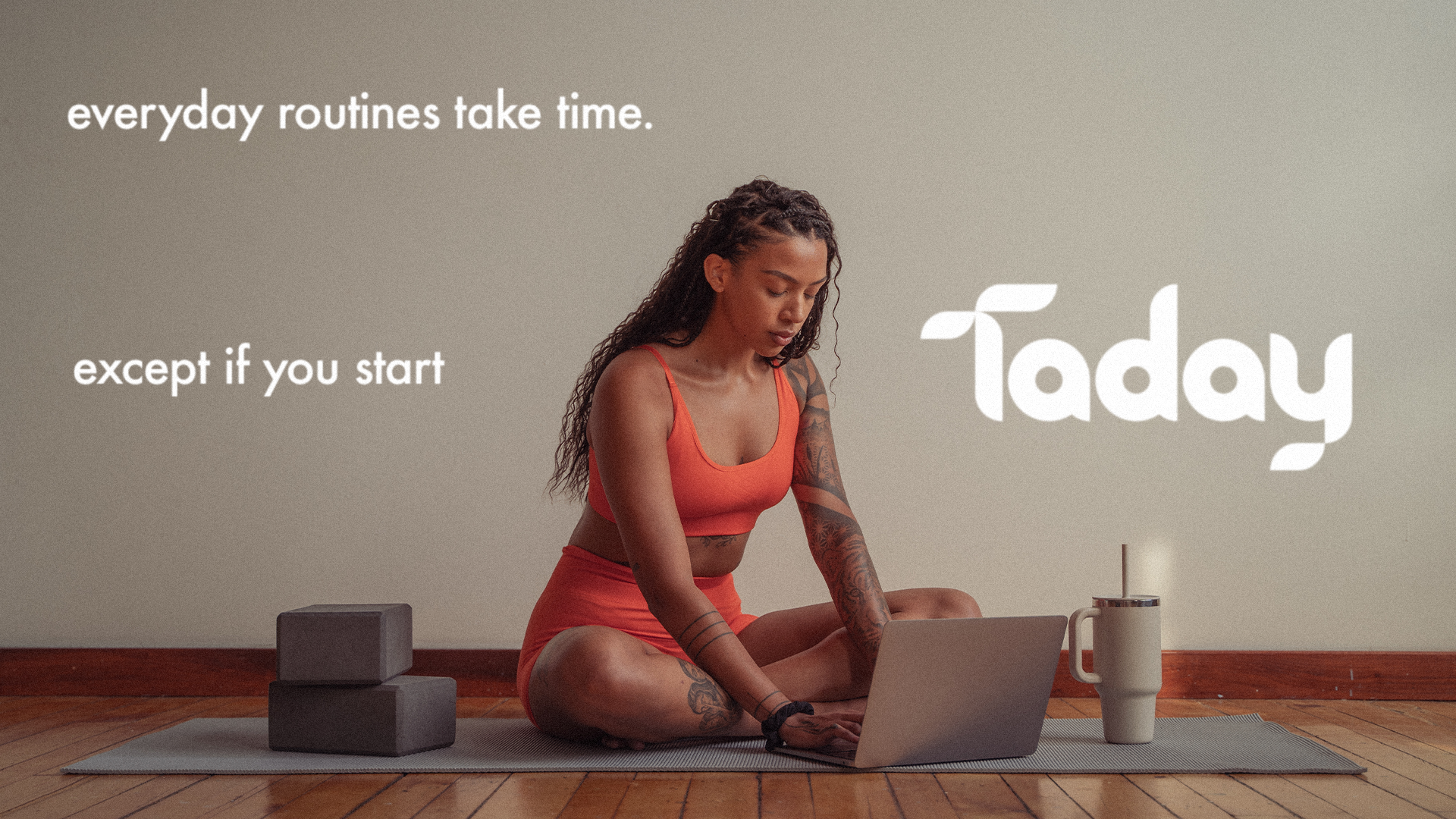 A woman practicing yoga indoors on a mat, sitting cross-legged with a laptop and a drink beside her, with yoga blocks nearby. The background has a motivational quote about routines and starting the day.