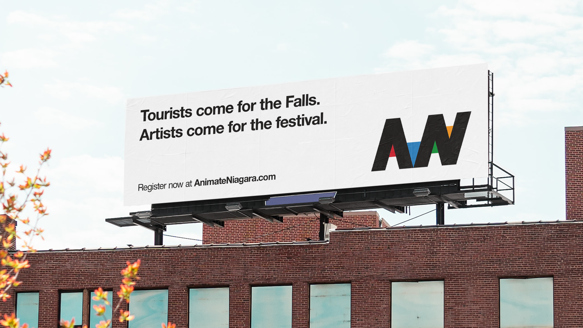 A large billboard on top of a brick building showing the text "Tourists come for the Falls. Artists come for the festival." and a logo with black, red, blue, green, and orange colors.