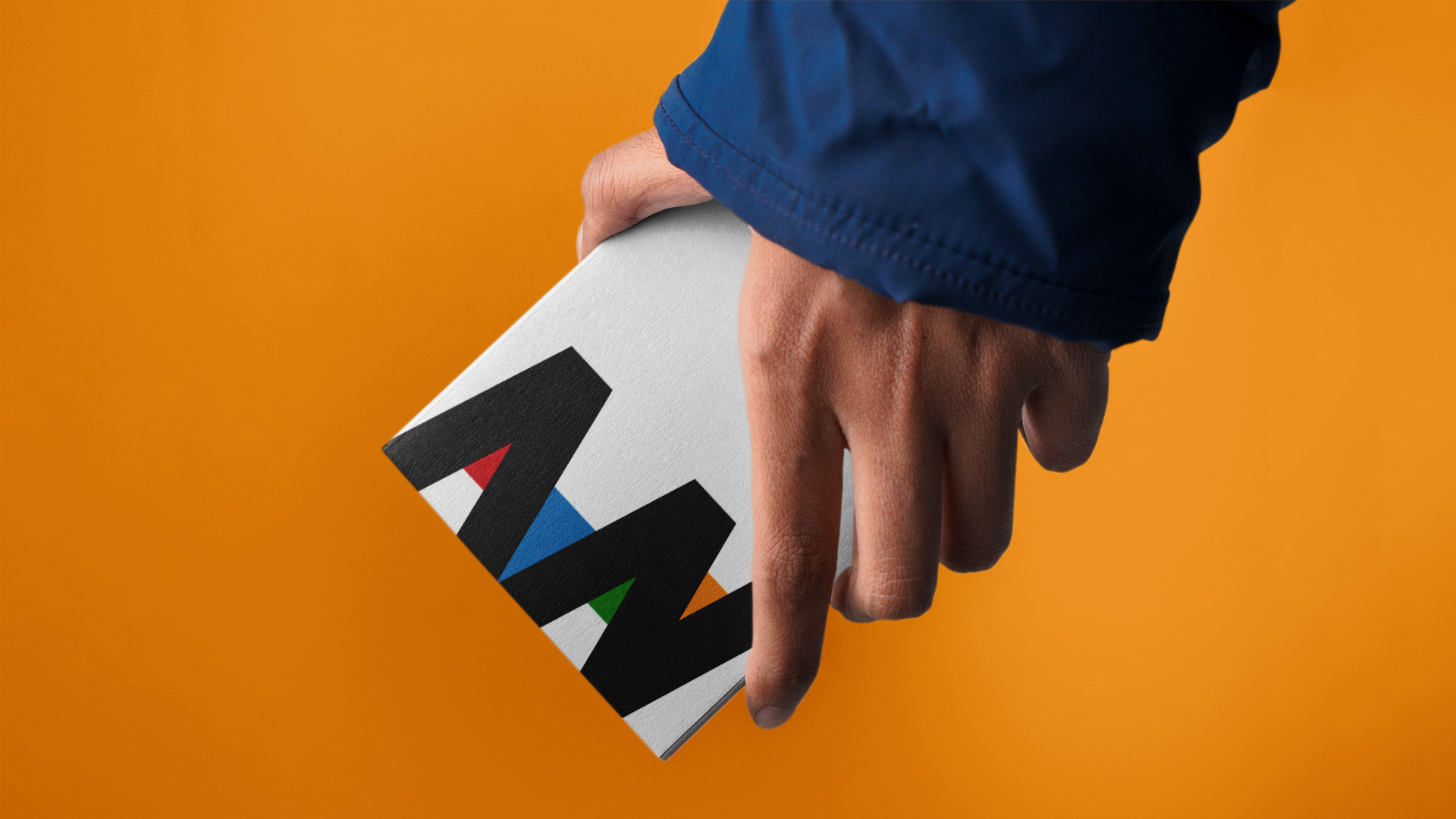 A hand with a blue sleeve holding a box with the 'AZ' logo against an orange background.