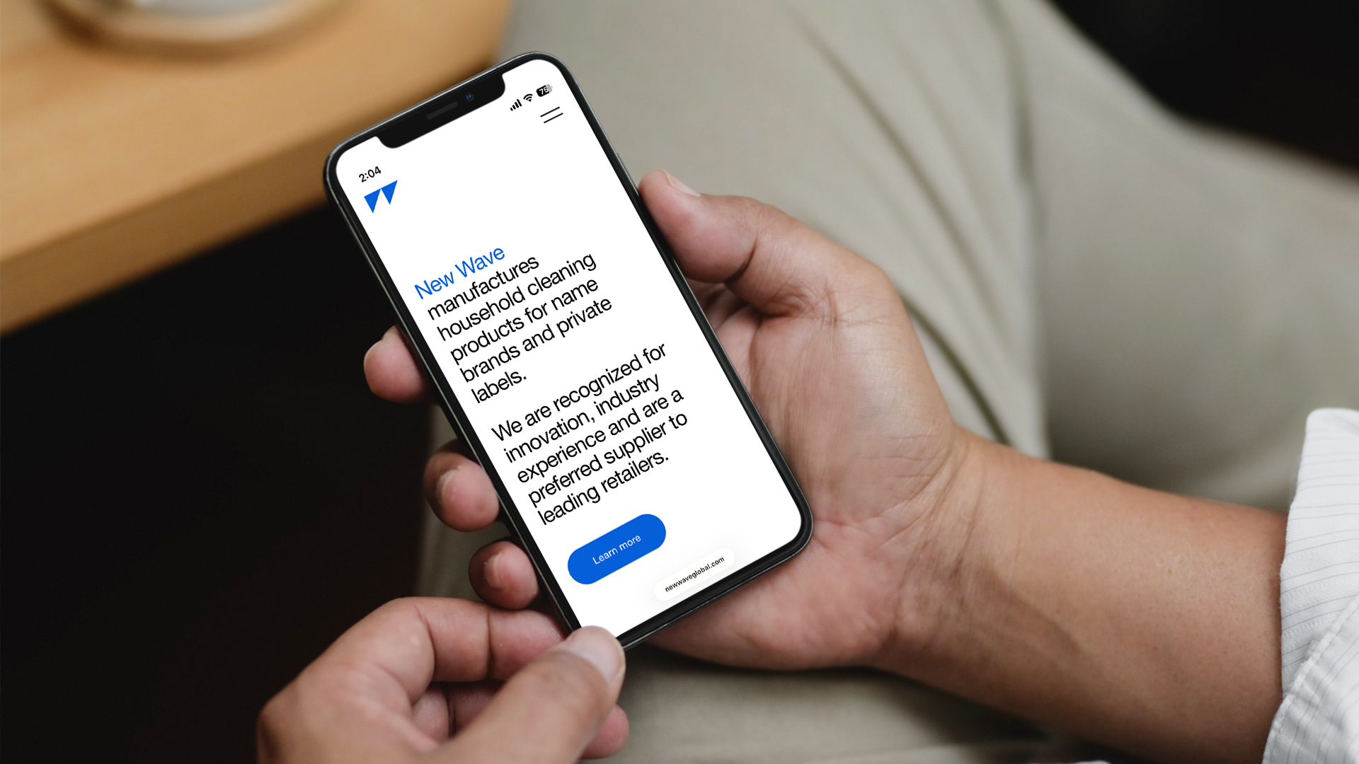 Person holding a smartphone with a webpage displayed about New Wave household cleaning products, featuring a blue 'Learn more' button.