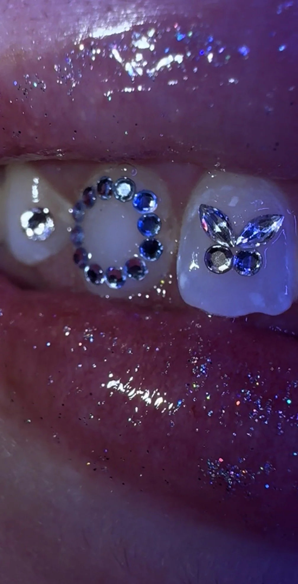 Close-up of a tongue decorated with shiny, jewel-like piercings and stickers, some in shapes like a circle, flower, and paddle boat.
