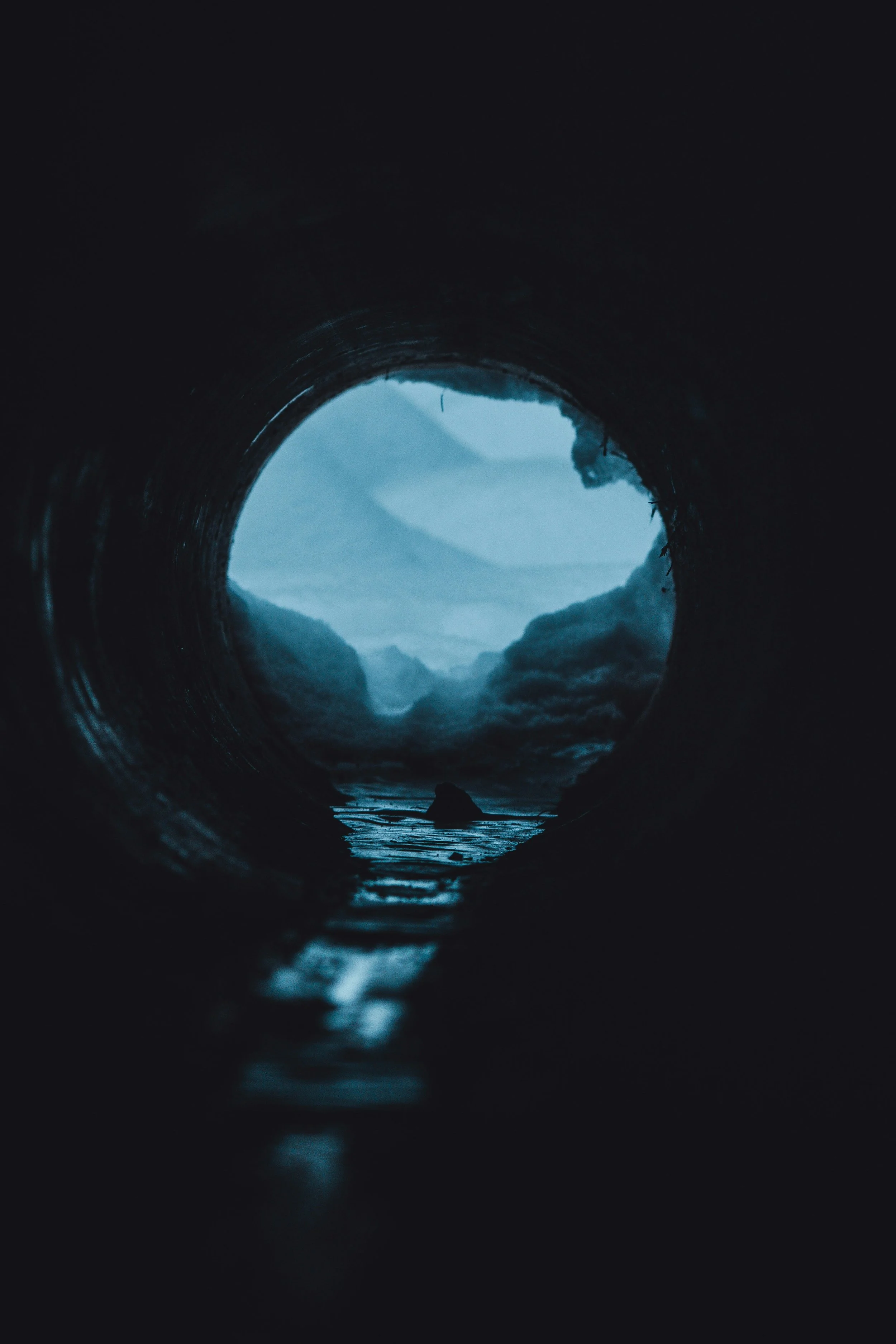 a dark tunnel reveals water and light on the other side
