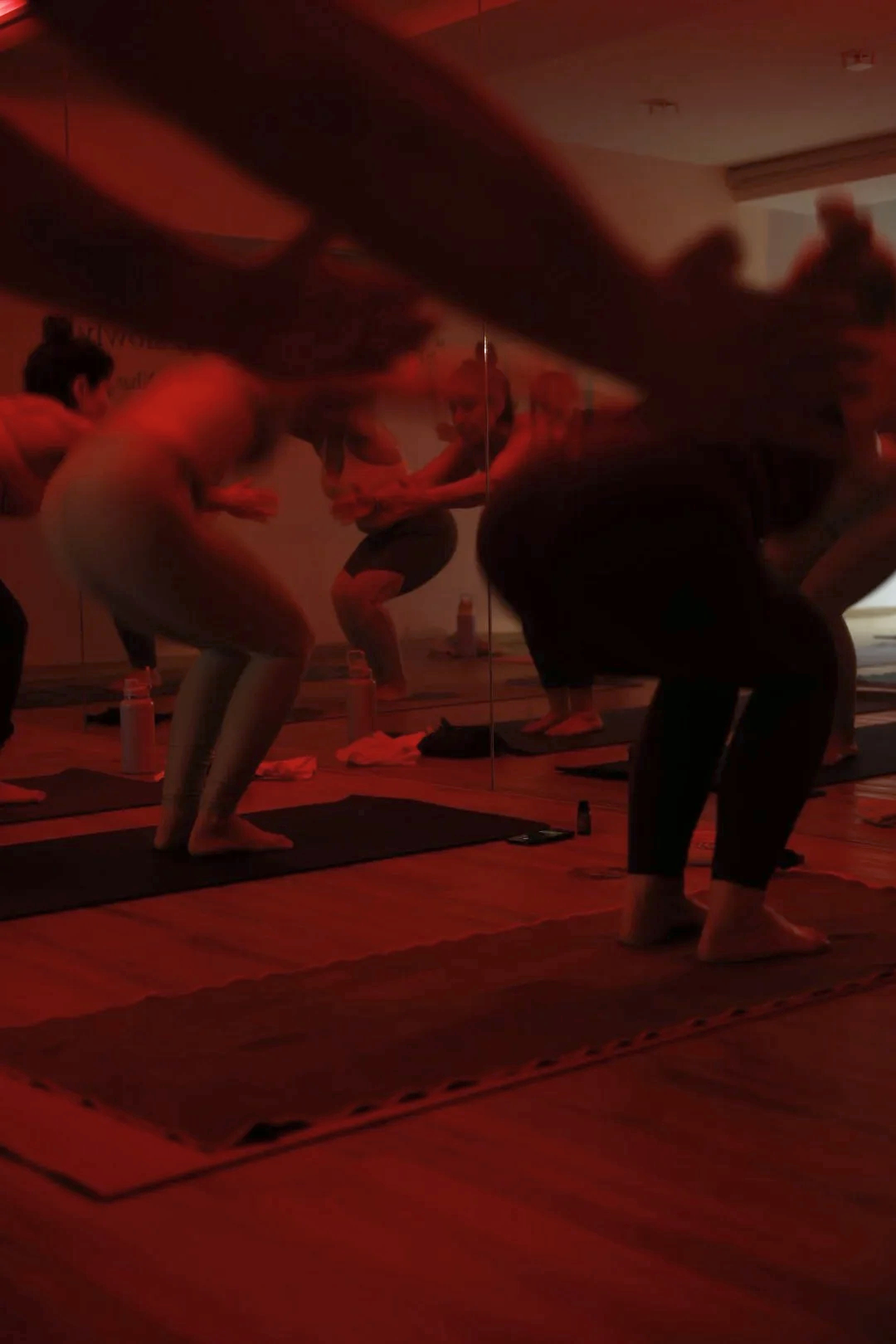 Grupo de personas realizando yoga en una clase en un estudio con iluminación tenue y pared de espejo.