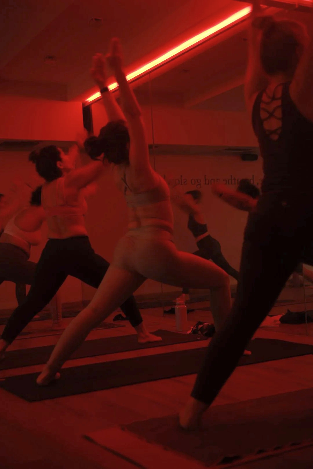 Personas practicando yoga en un estudio, en una sala con iluminación roja y pared de espejos.