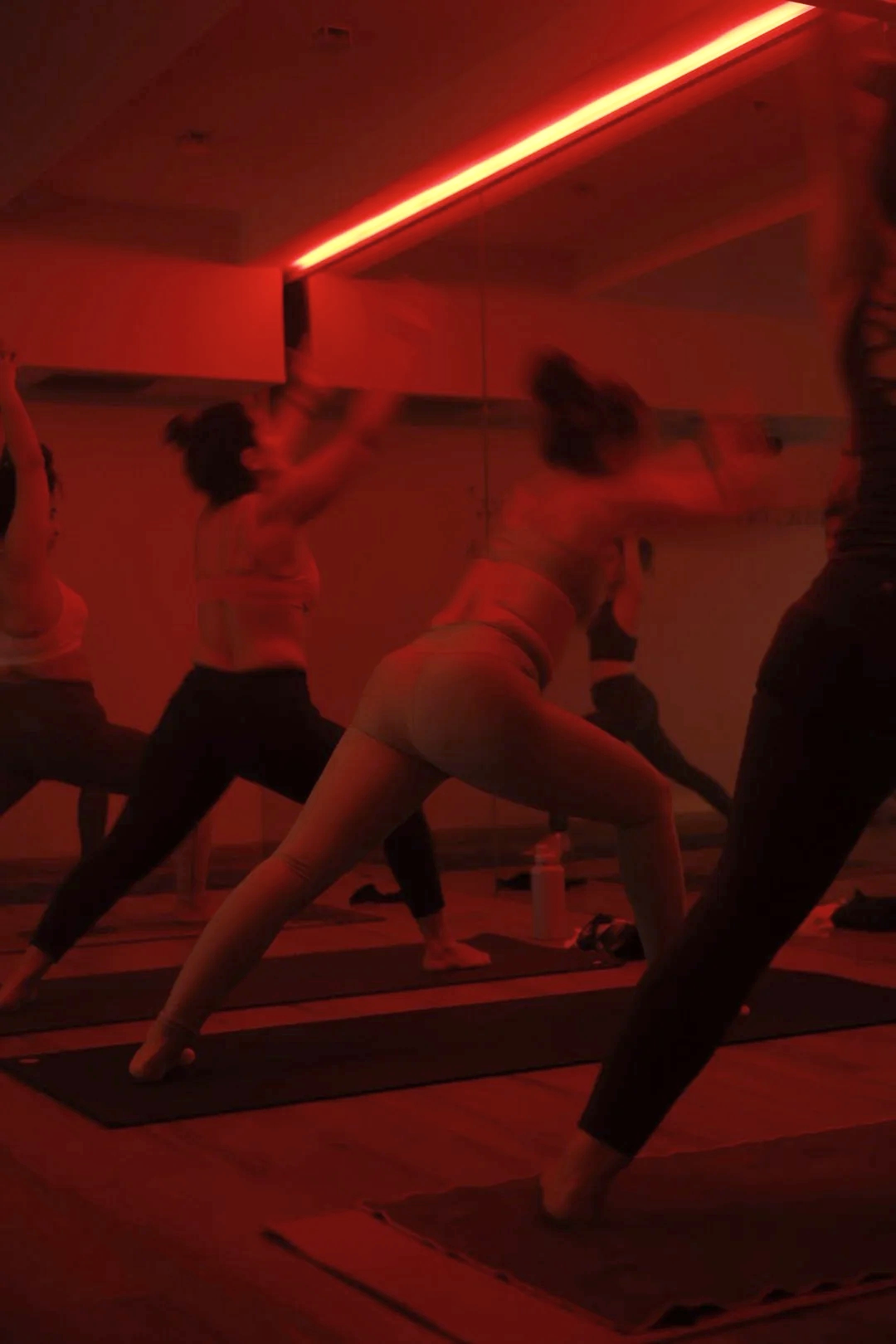 Grupo de personas haciendo yoga en una sala con iluminación roja.