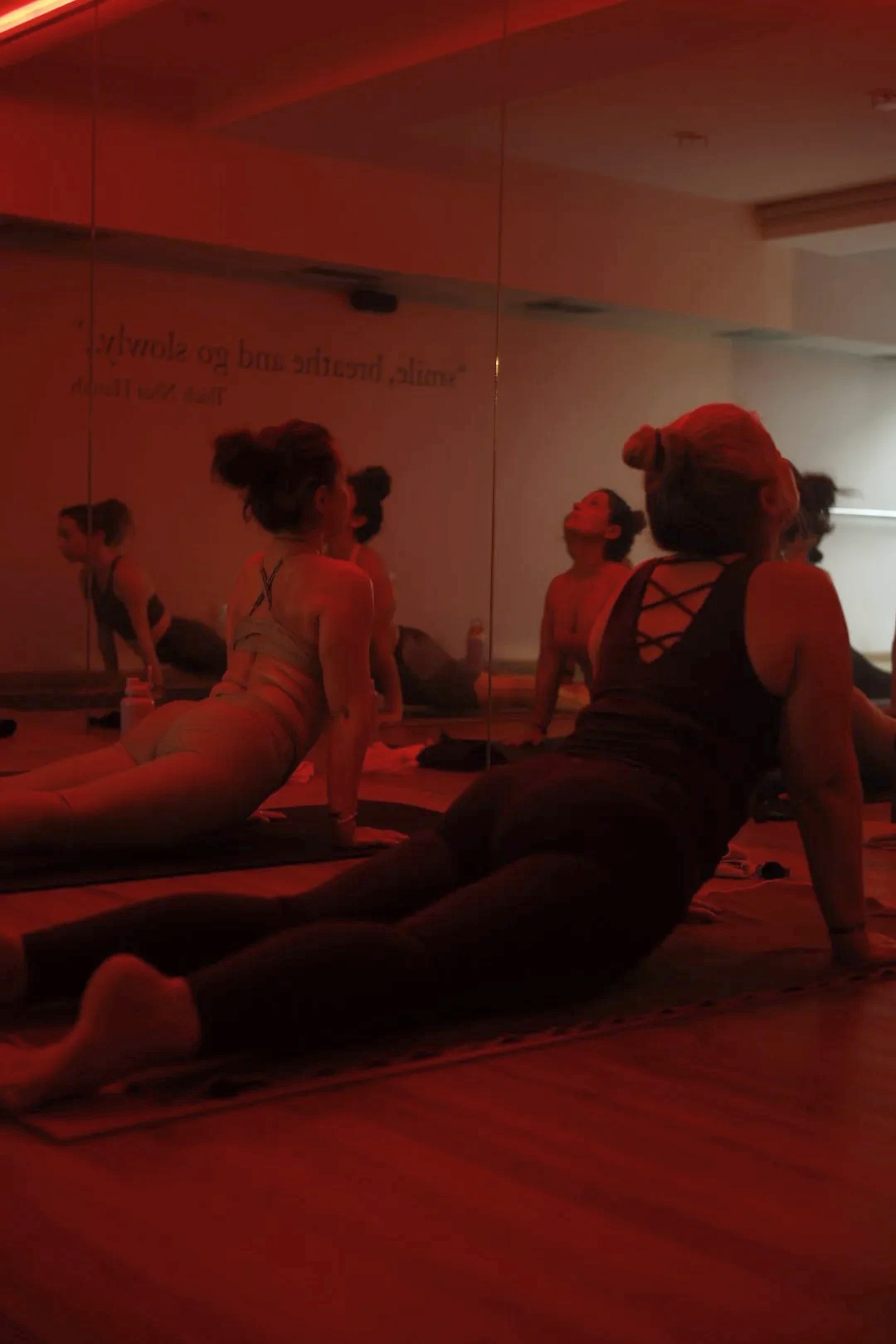Personas haciendo yoga en un estudio con paredes de espejo y ambiente de luz tenue y roja.