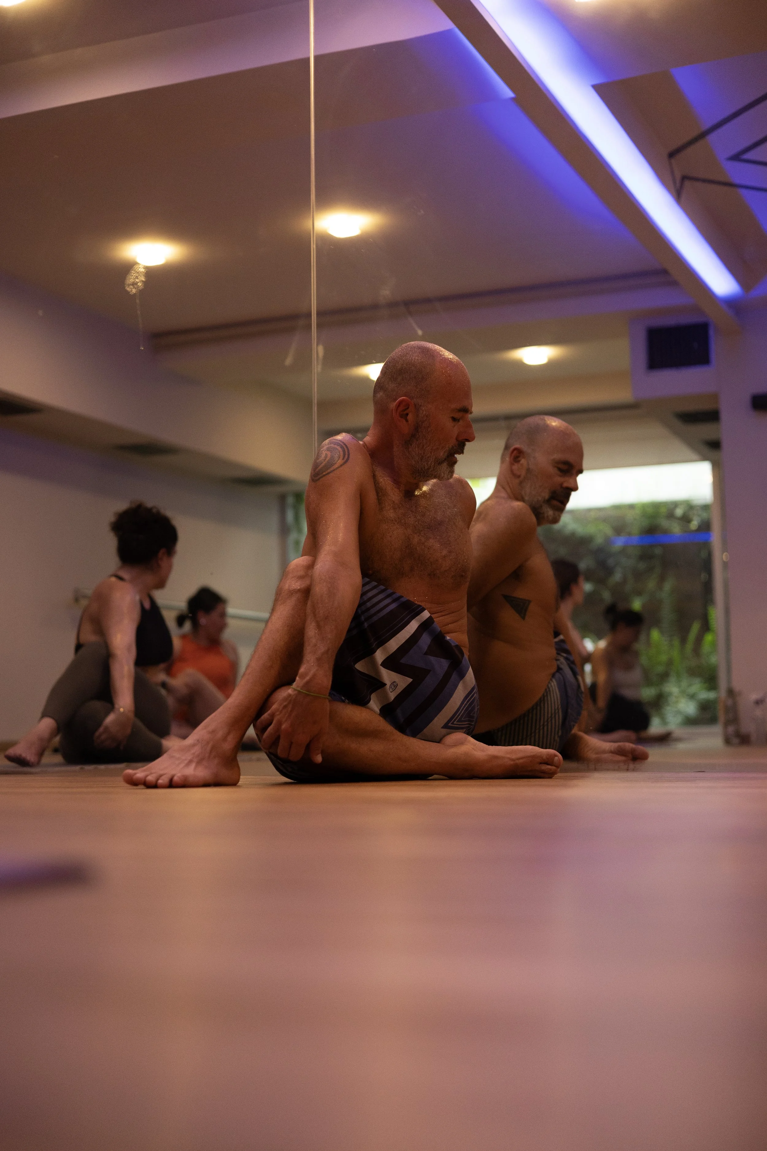 Hombres mayores practicando yoga en una clase, en postura de yoga en el suelo en un estudio con iluminación suave.