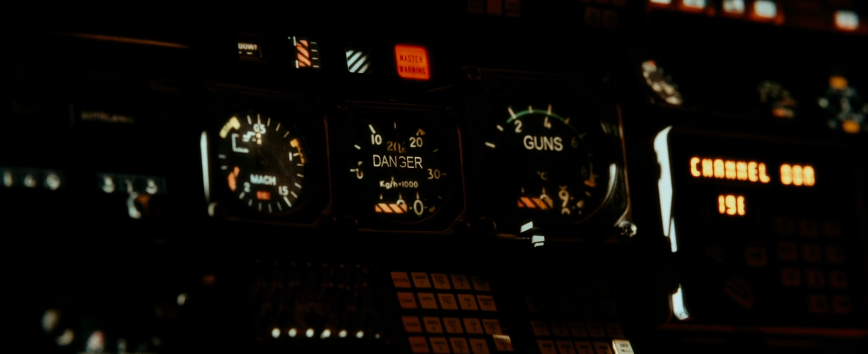 Dimly lit airplane cockpit instrument panel with gauges, warning lights, illuminated control buttons, and a digital display