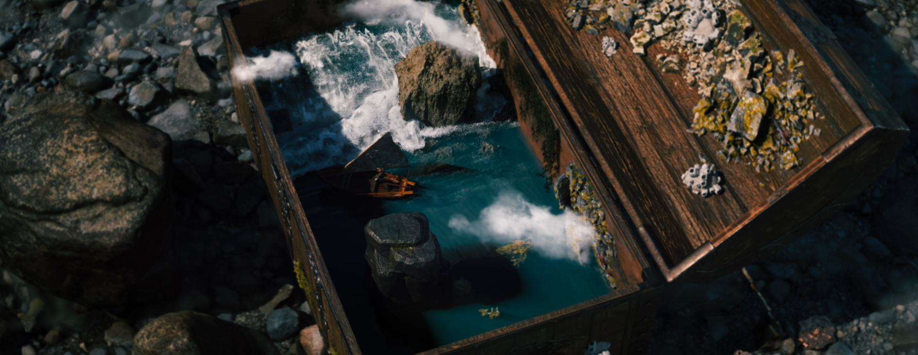 Top-down view of a miniature wooden watermill with rushing blue water, rocks, and moss-covered details